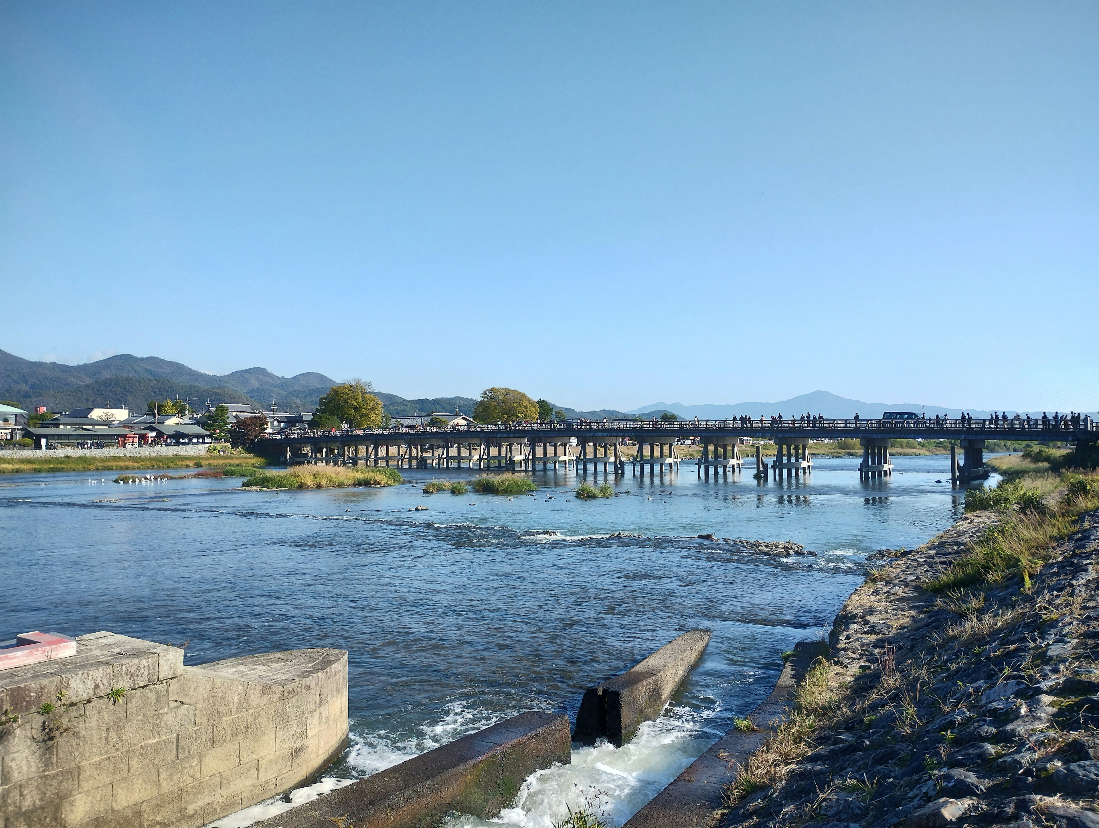 Pemandangan sungai yang tenang dengan jembatan gunung di latar belakang langit biru cerah