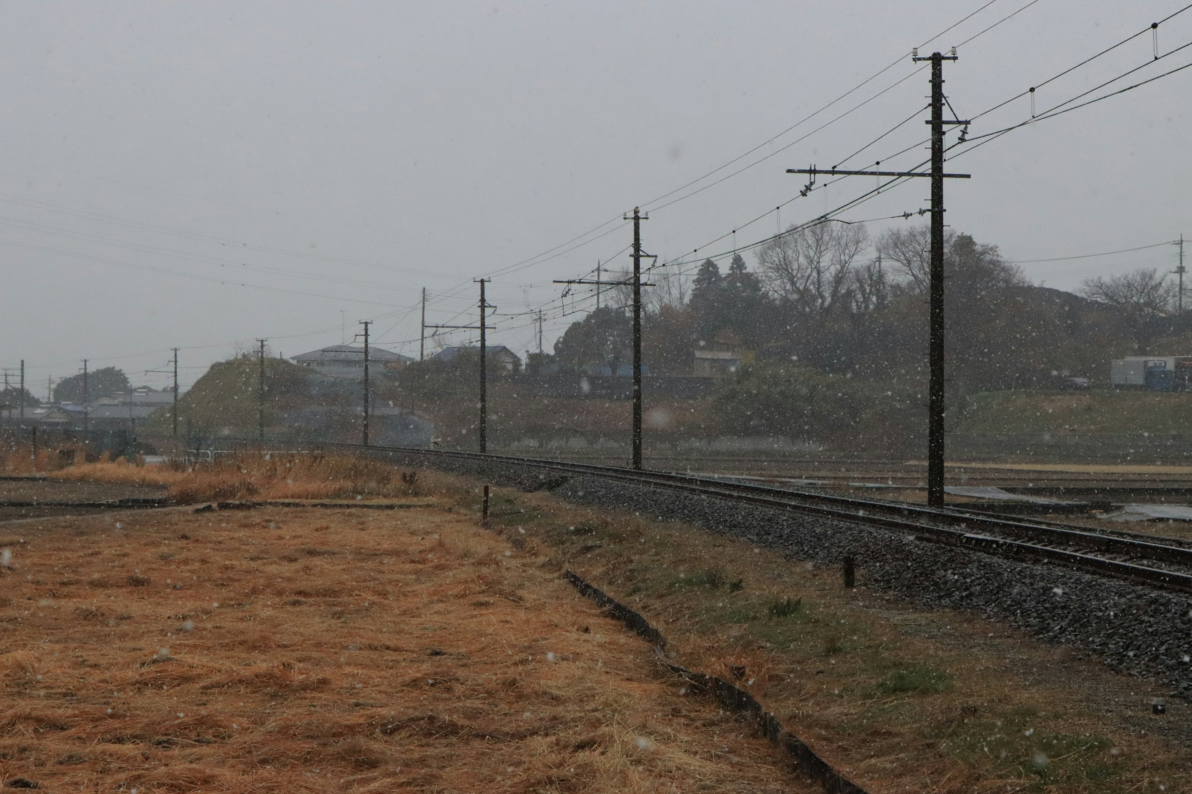 Binari ferroviari e pali elettrici in un paesaggio piovoso