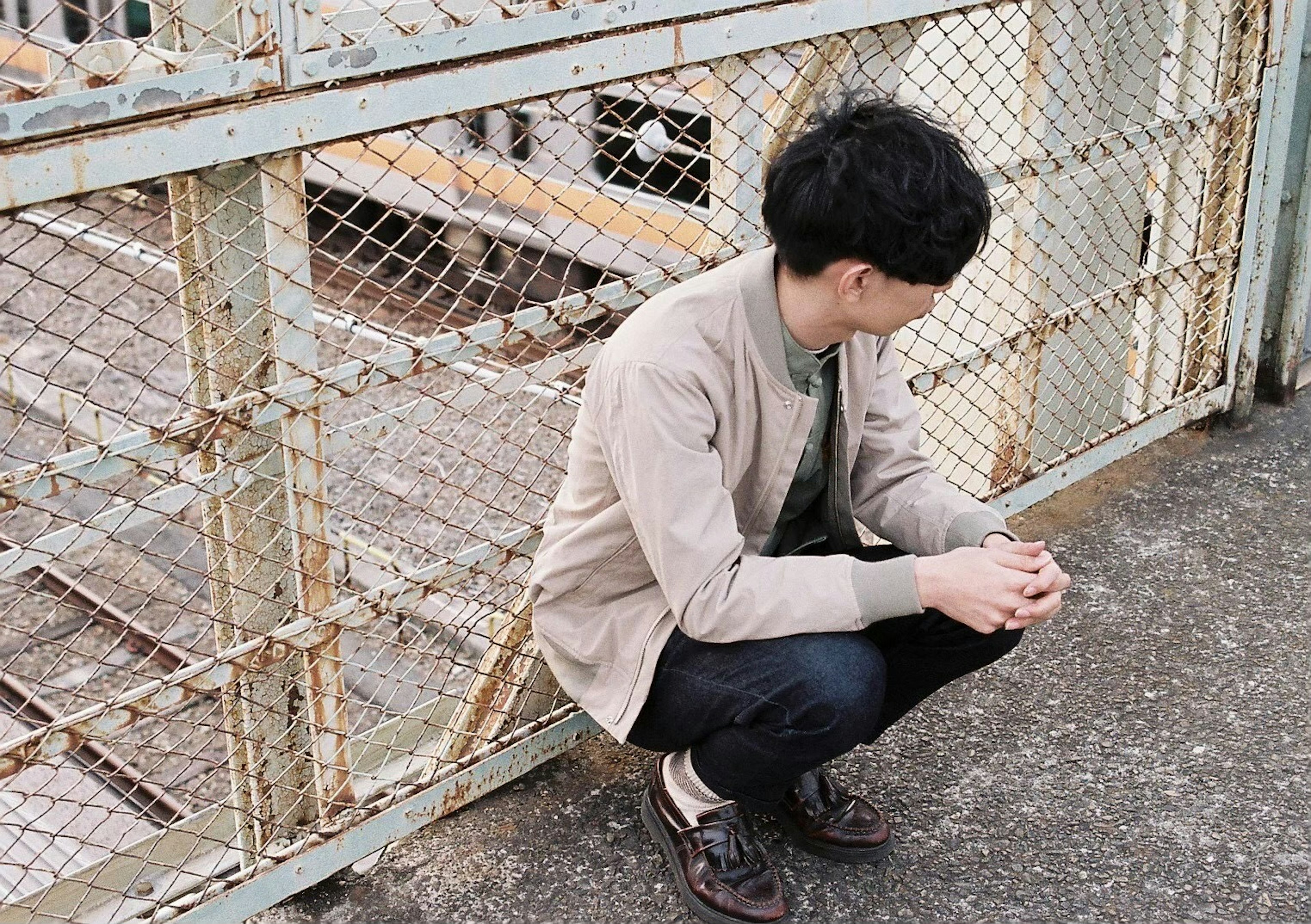 A young man squatting in front of a metal fence