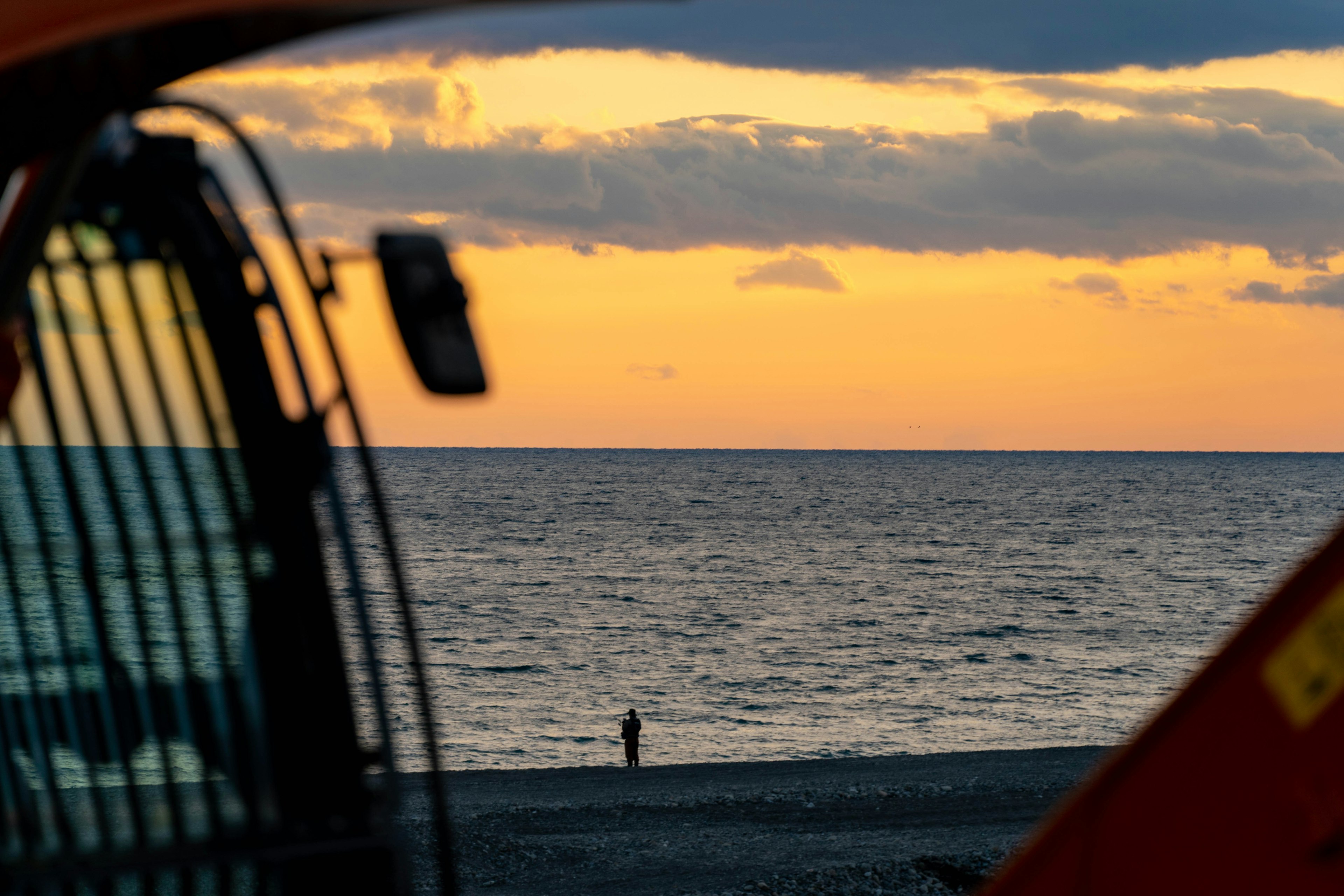 夕焼けの海を背景に立つ人影とオレンジの機械