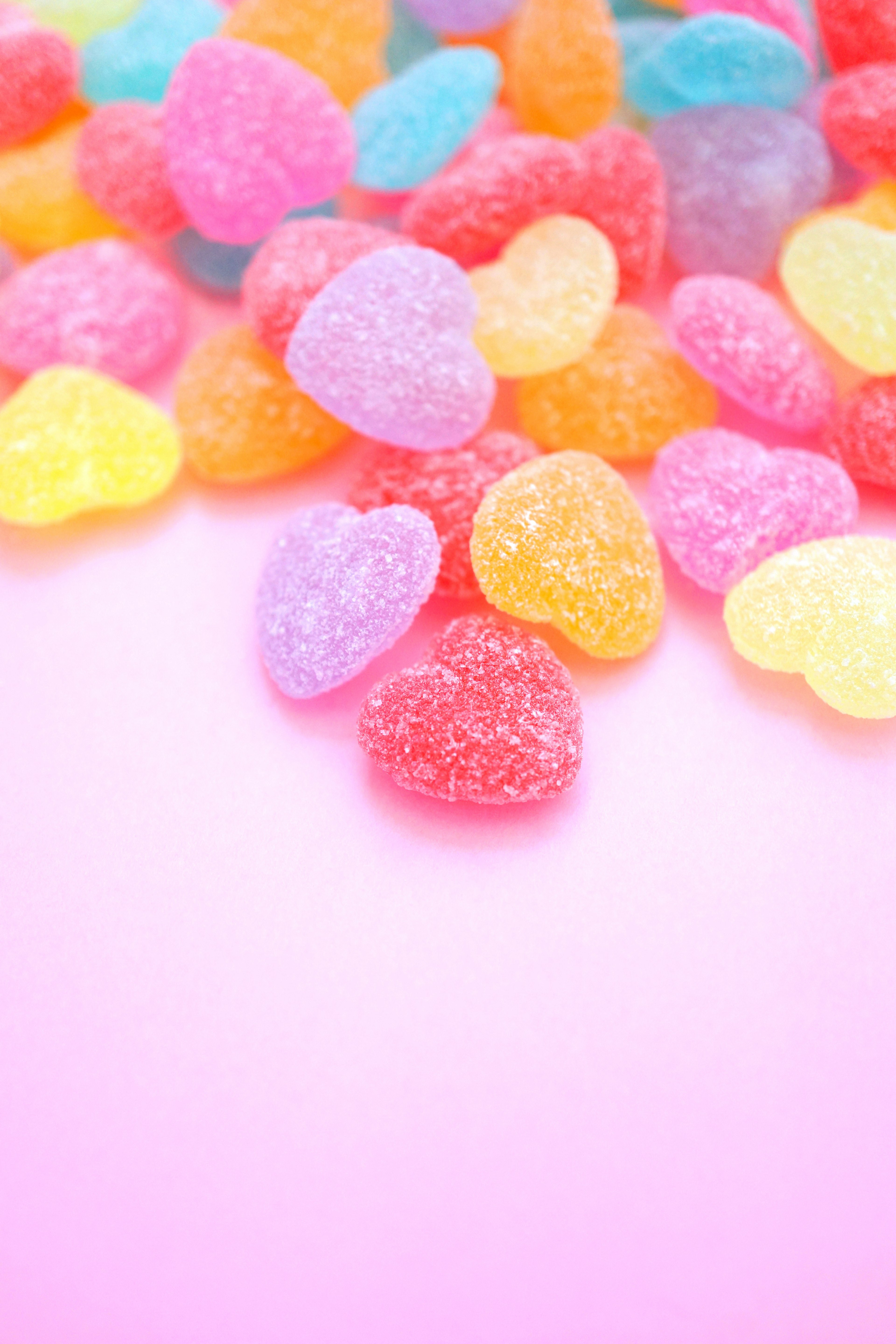 Caramelos de goma en forma de corazón de colores esparcidos sobre un fondo rosa