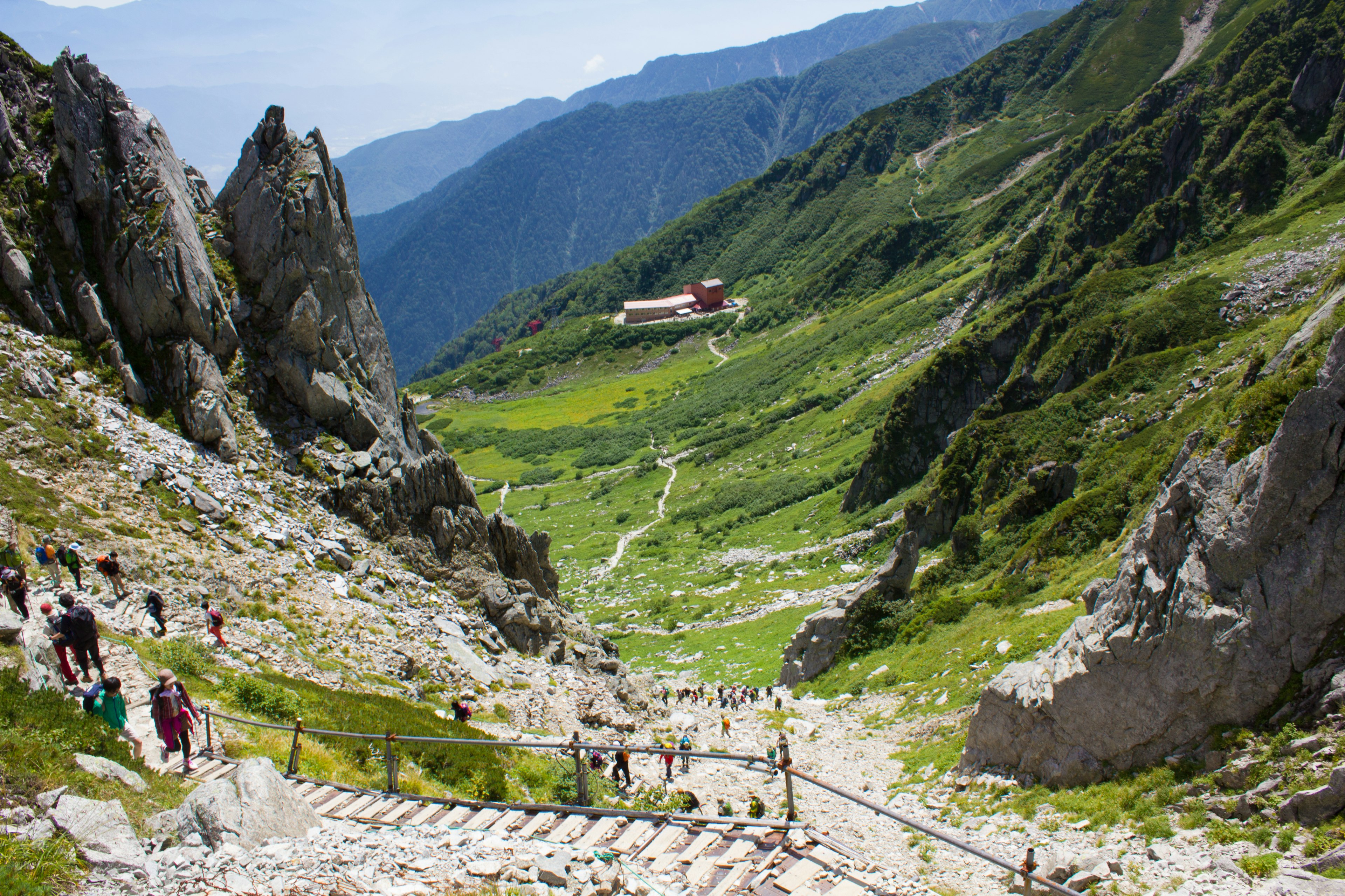 Vallée de montagne pittoresque avec des randonneurs marchant sur le chemin chalet de montagne au loin