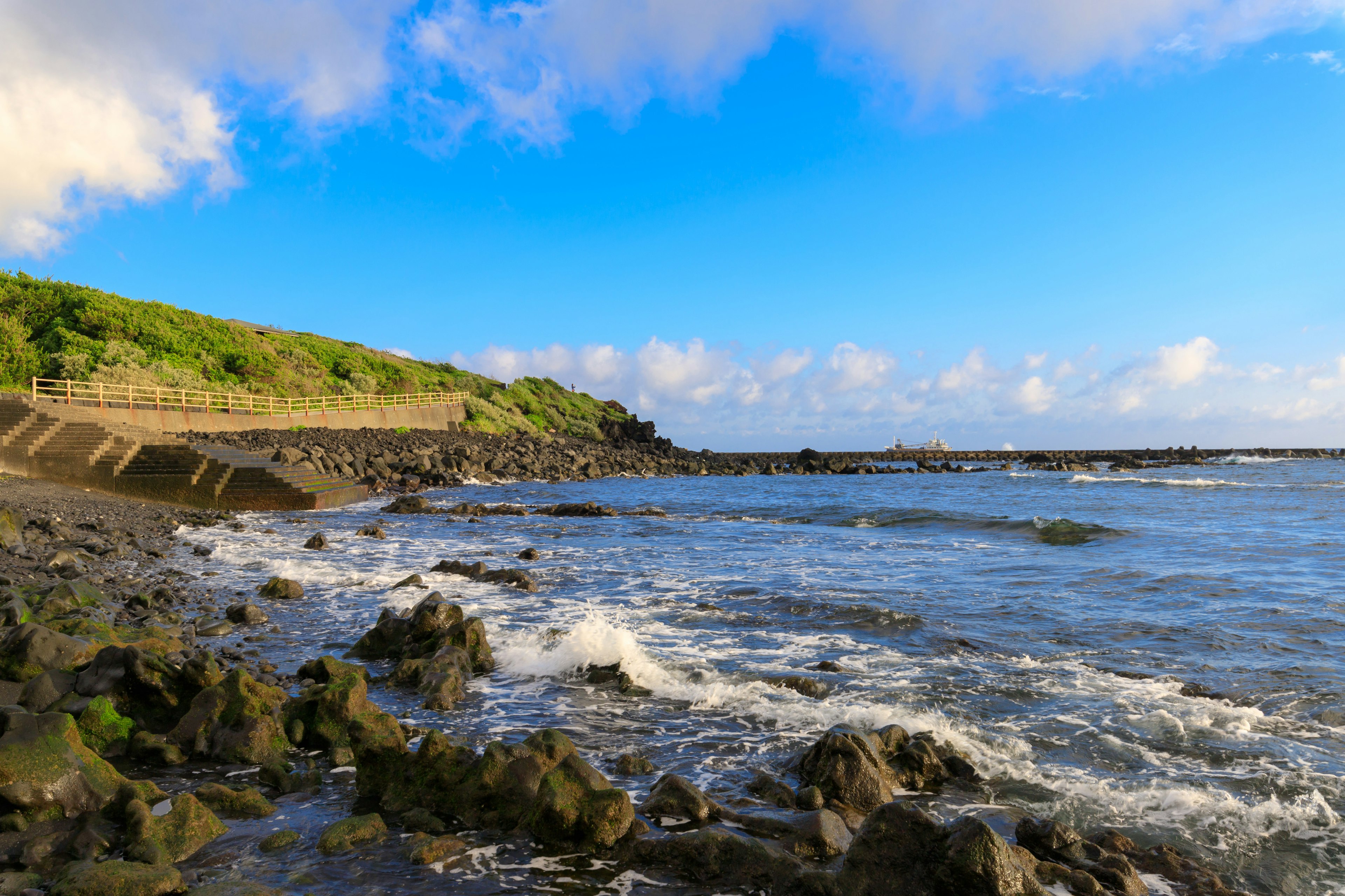 Küstenlandschaft mit blauem Himmel und weißen Wolken Wellen schlagen gegen Felsen