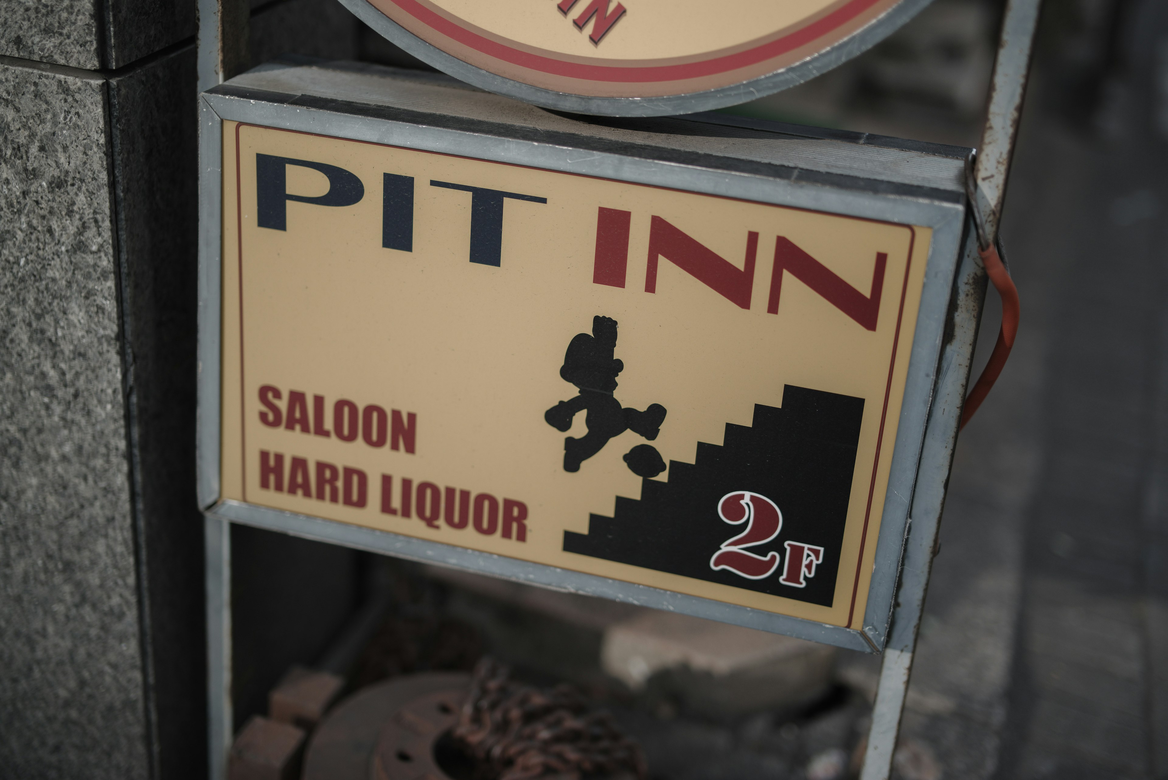 Sign for Pit Inn featuring a person climbing stairs with text for saloon and hard liquor