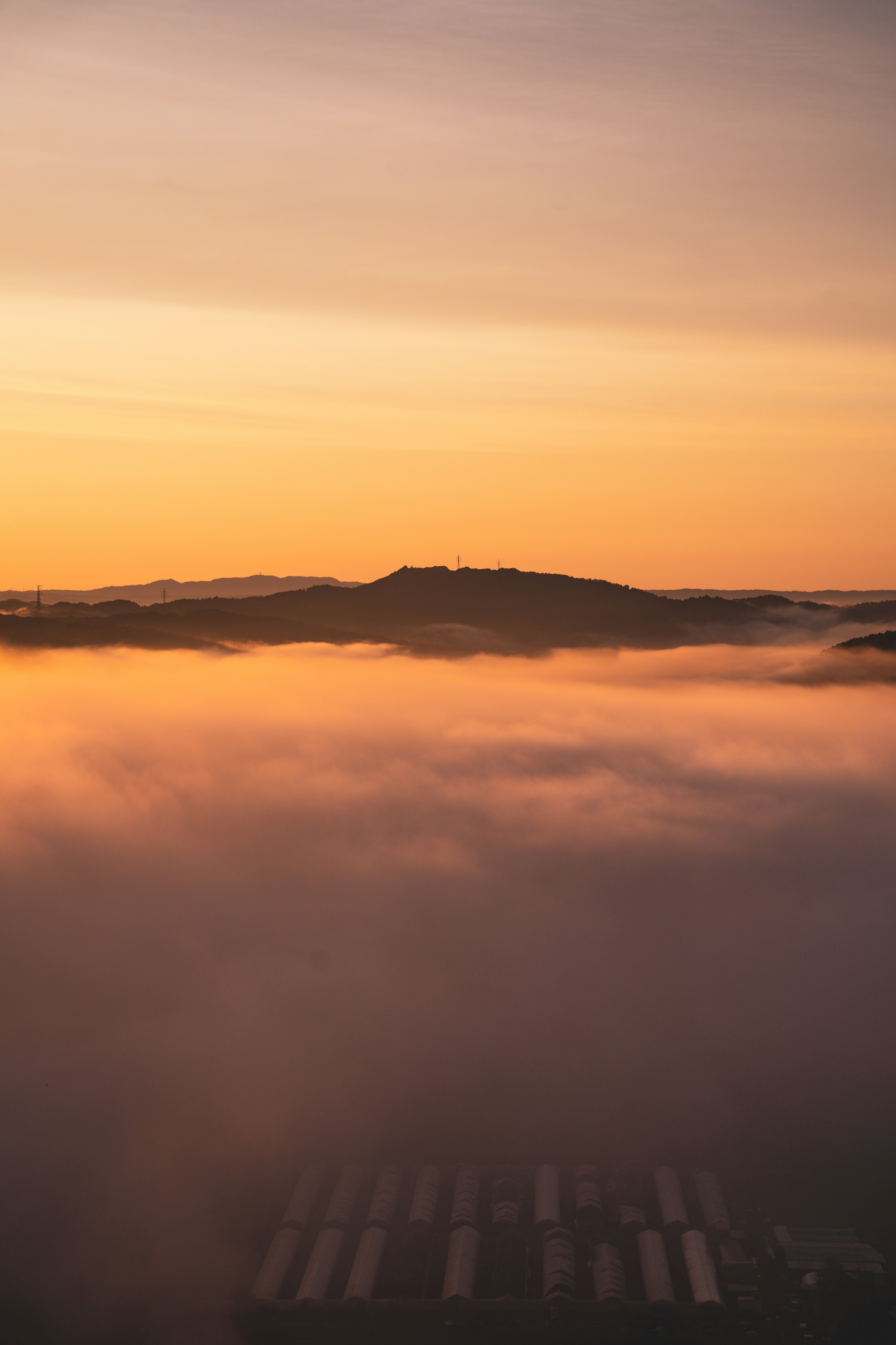 Sommet de montagne entouré de brouillard avec un coucher de soleil orange