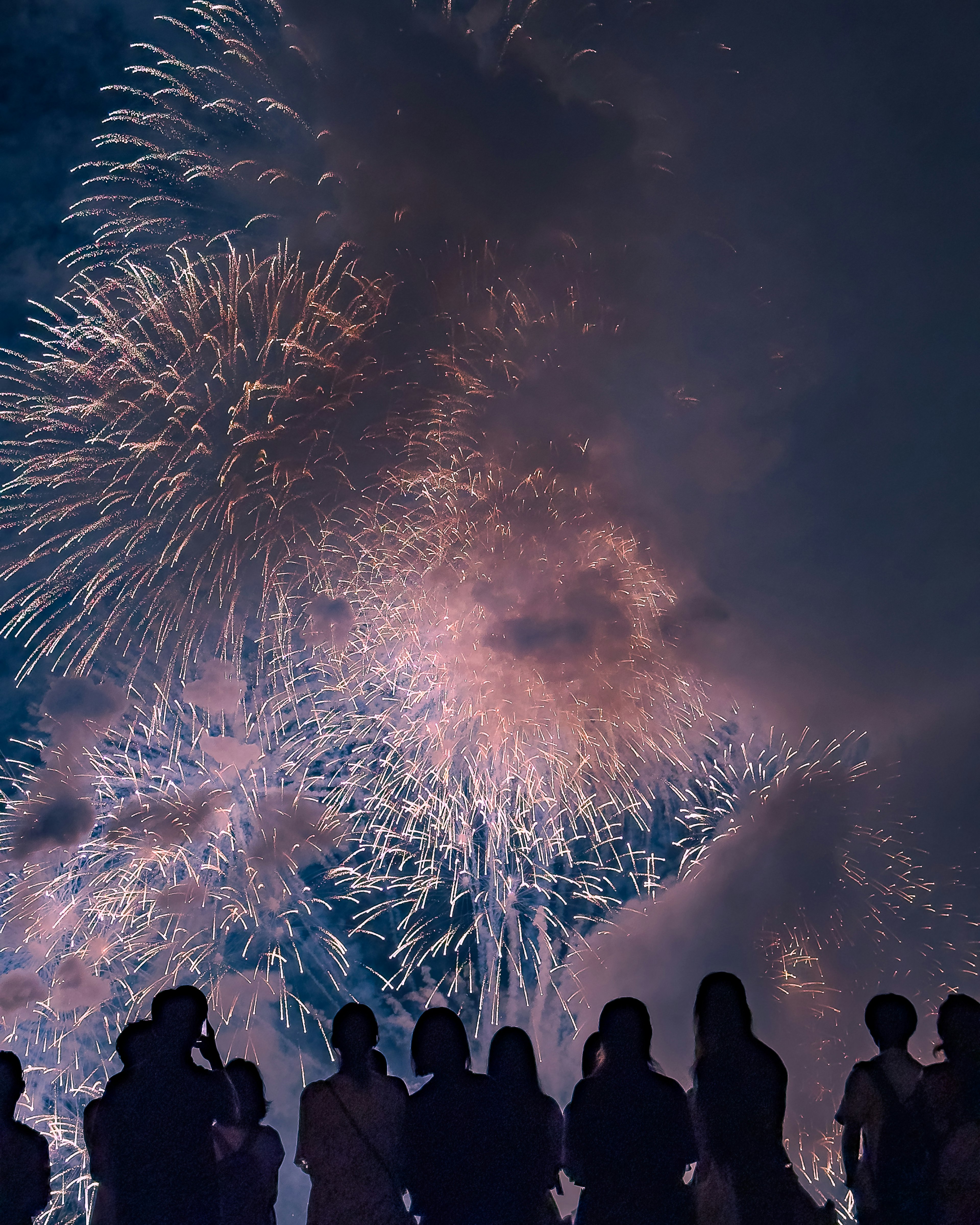 夜空に広がる花火とシルエットの人々