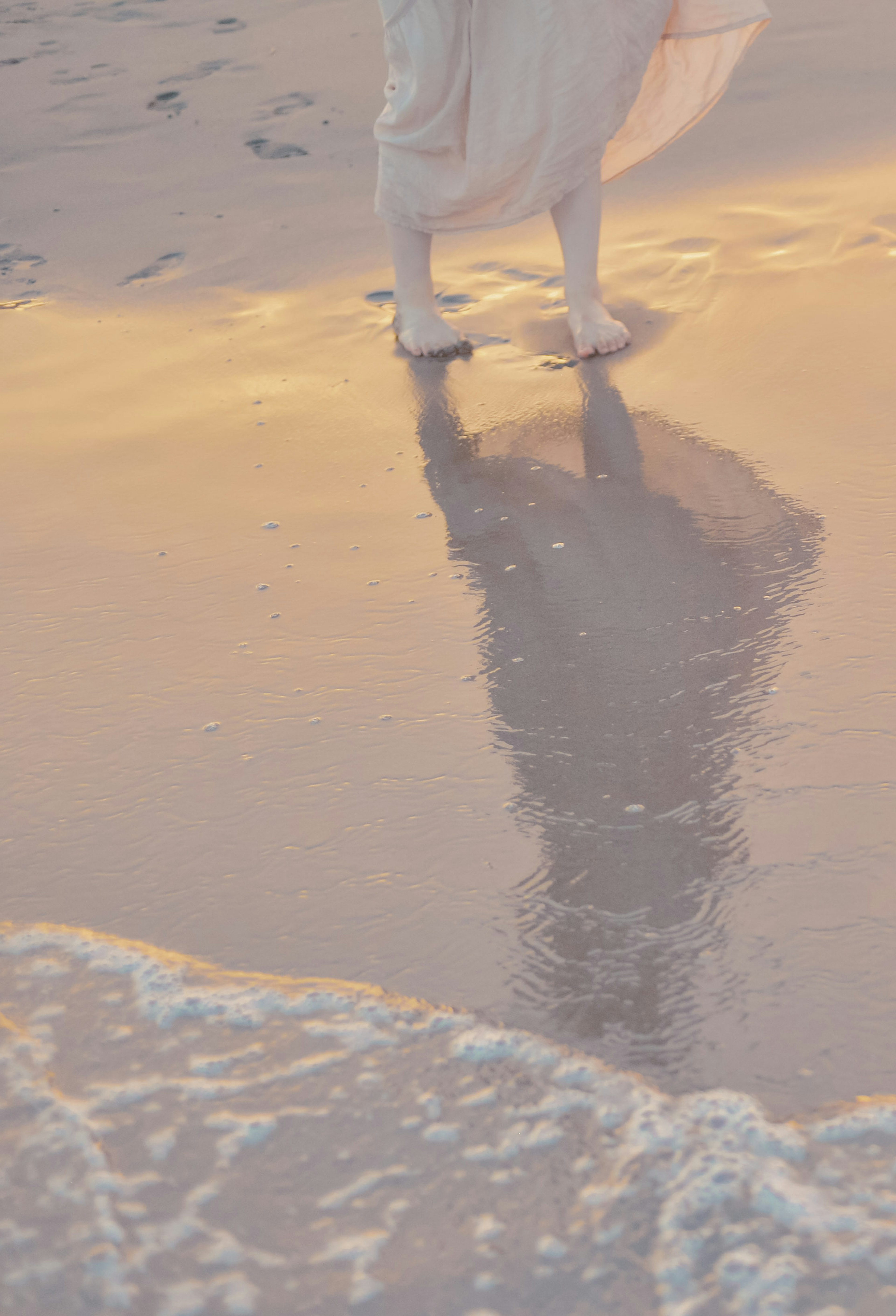 Pies con atuendo blanco proyectando un reflejo en la arena mojada de la playa