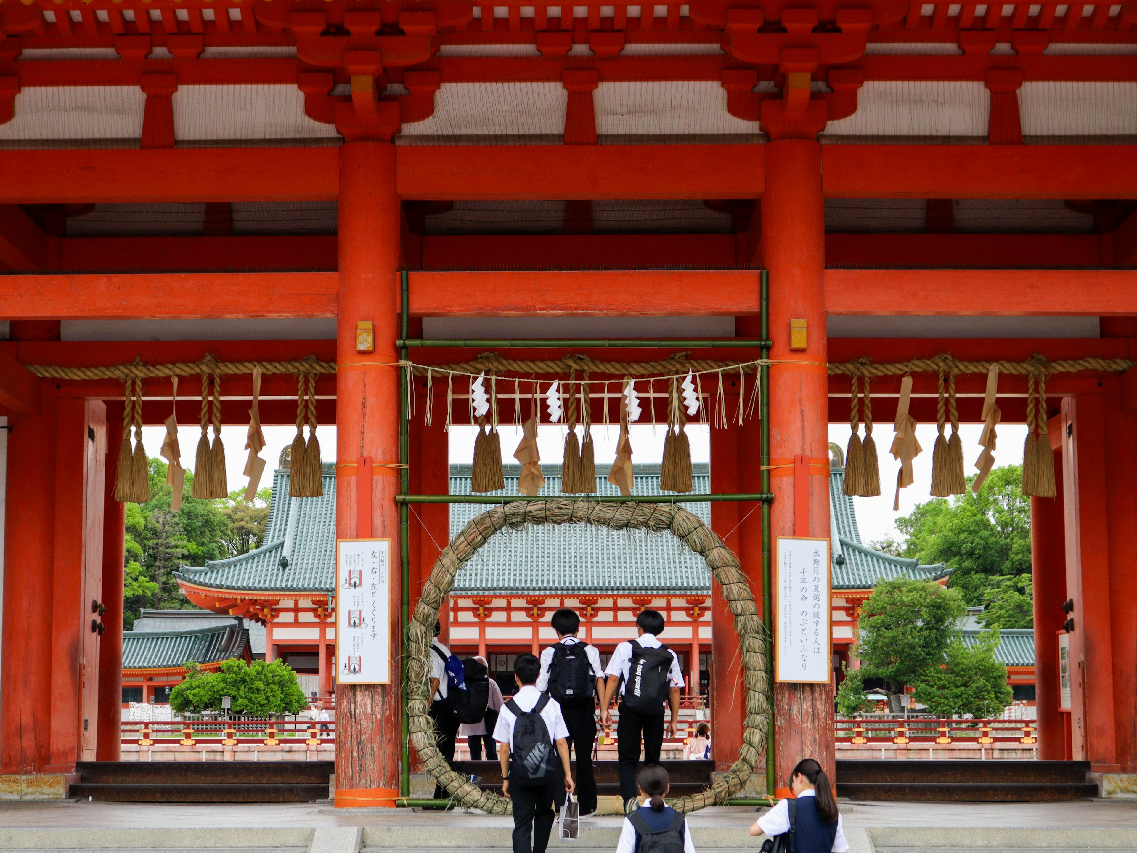 赤い門と注連縄を持つ神社の前で学生たちが行き交う風景