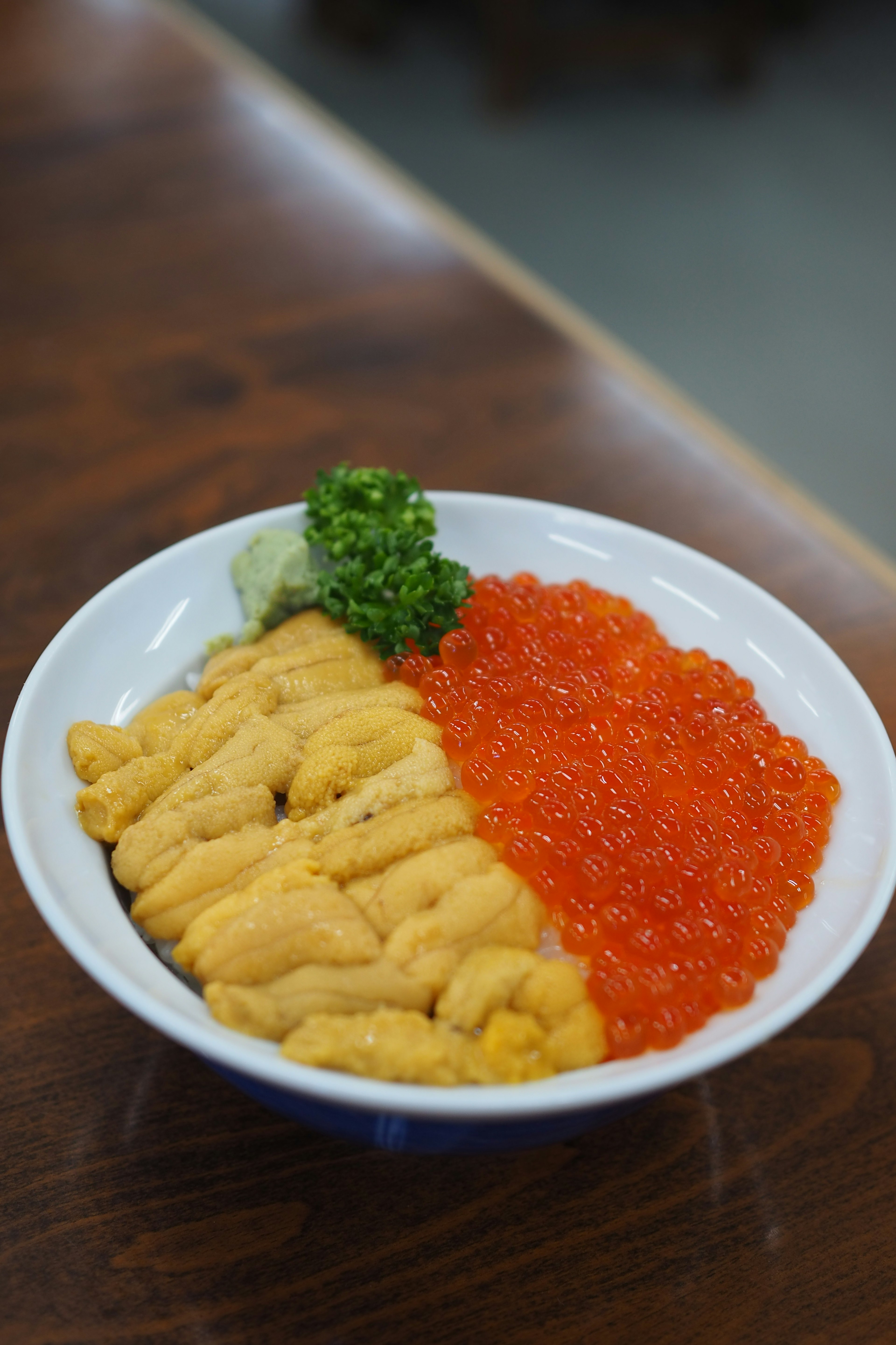 Schale mit Seeigel und Lachsrogen mit grünem Wasabi und Blättern in einer weißen Keramikschale