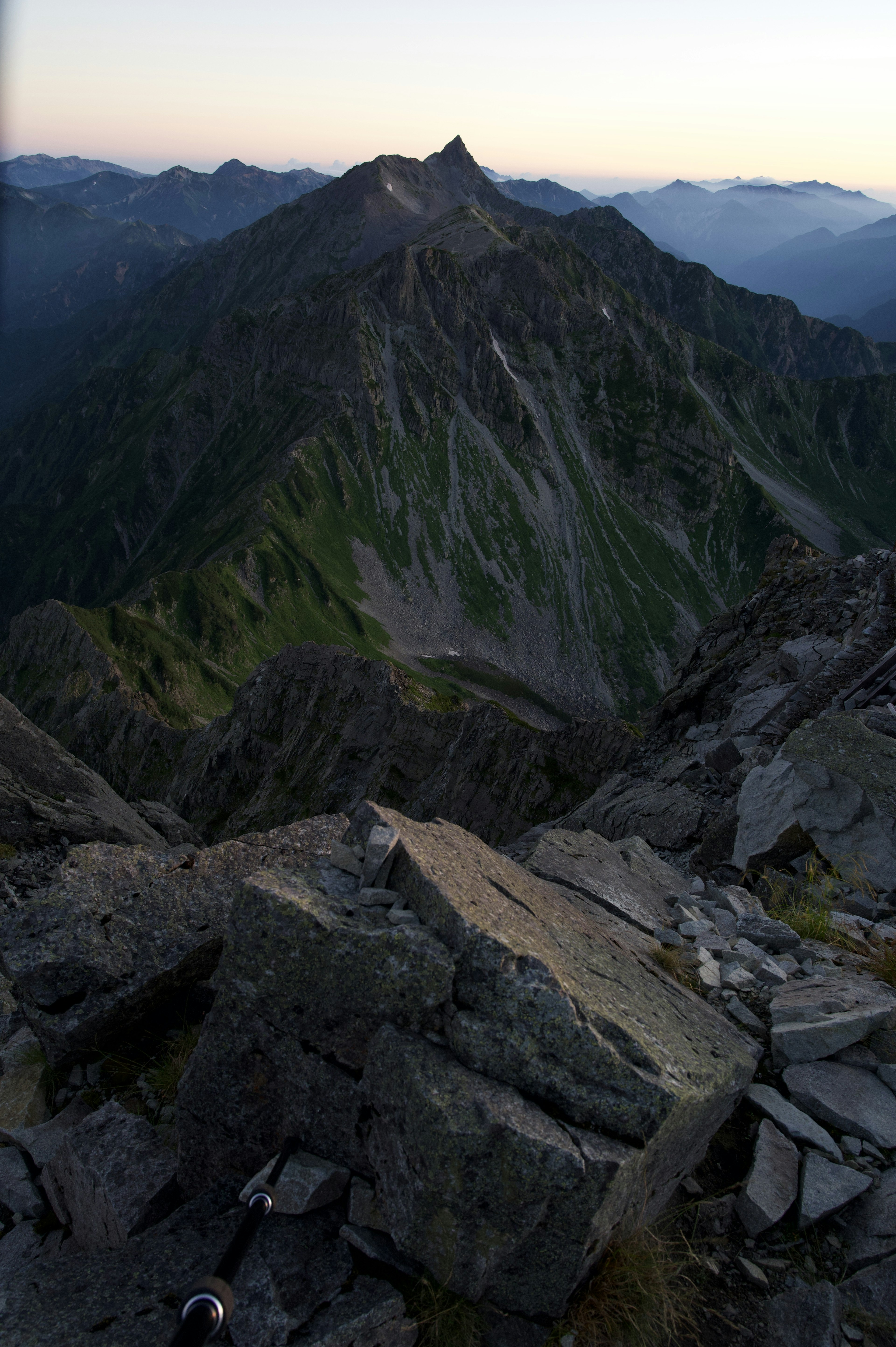 View from mountain peak showing green slopes and rocky formations