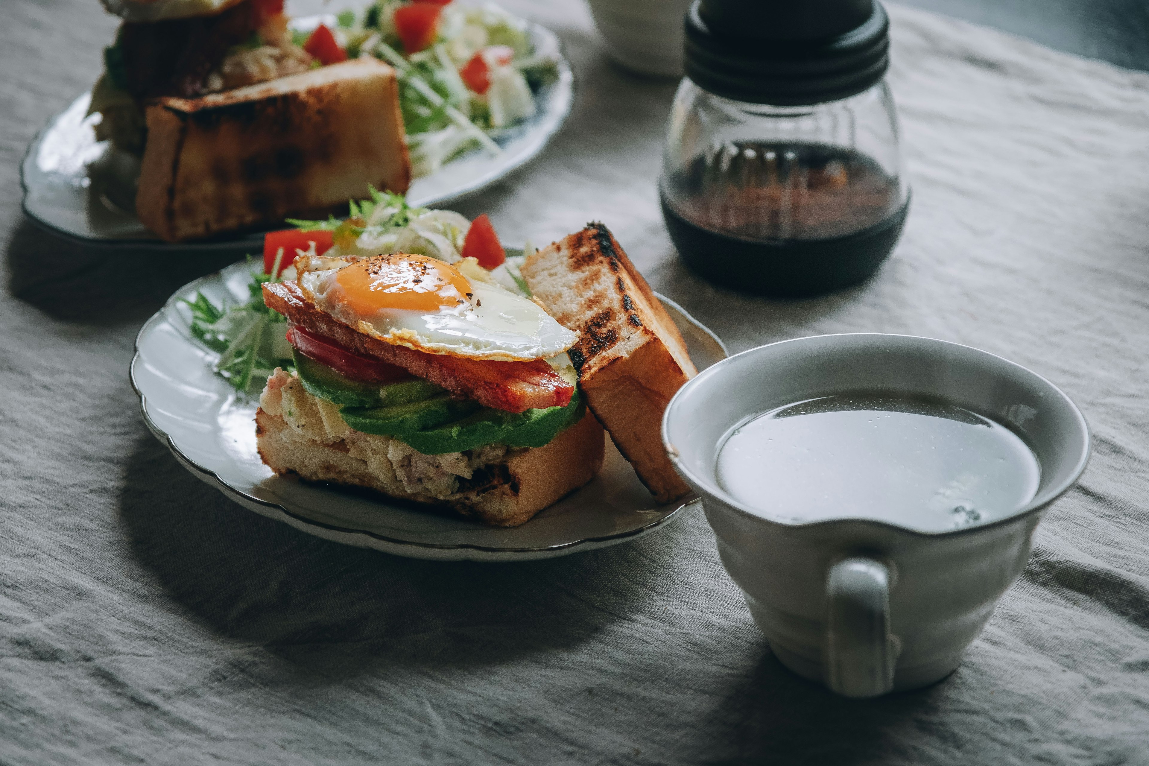 Sarapan dengan sandwich yang ditambahkan telur goreng dan sayuran disertai secangkir kopi