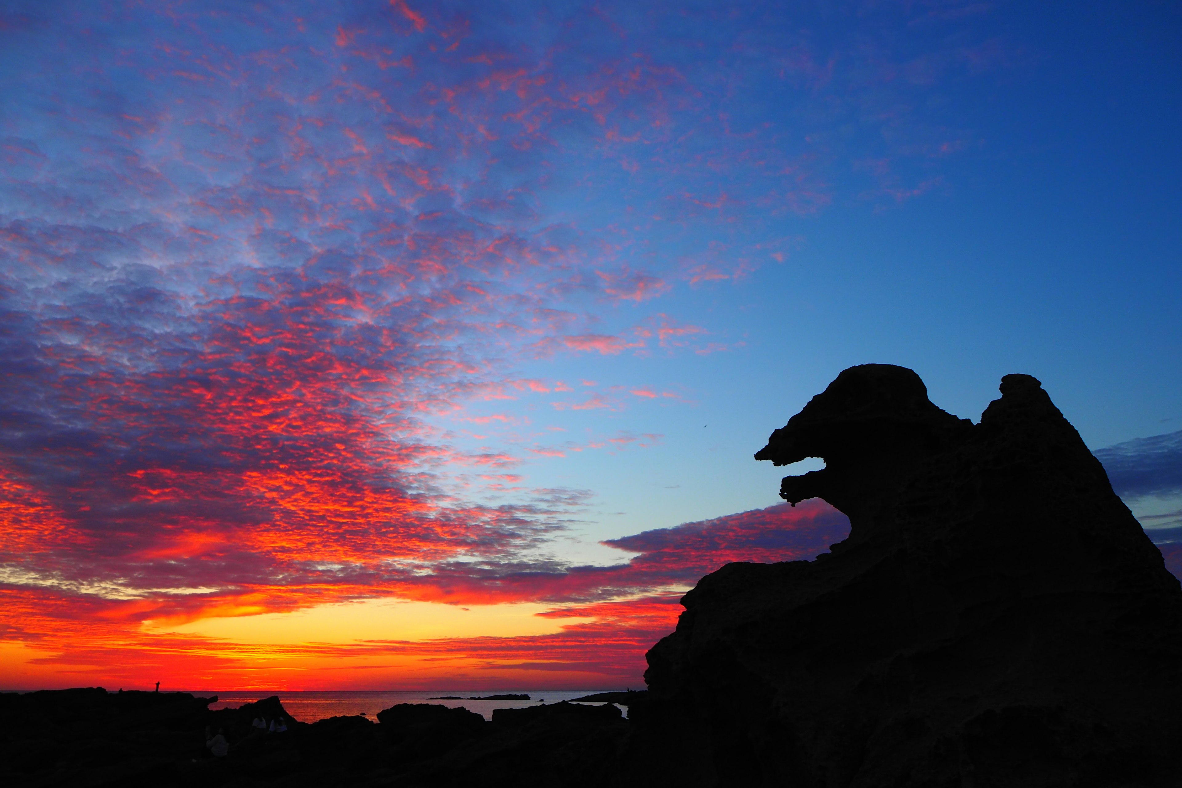 夕焼けの空のシルエットに見える岩の形が獅子のように見える風景