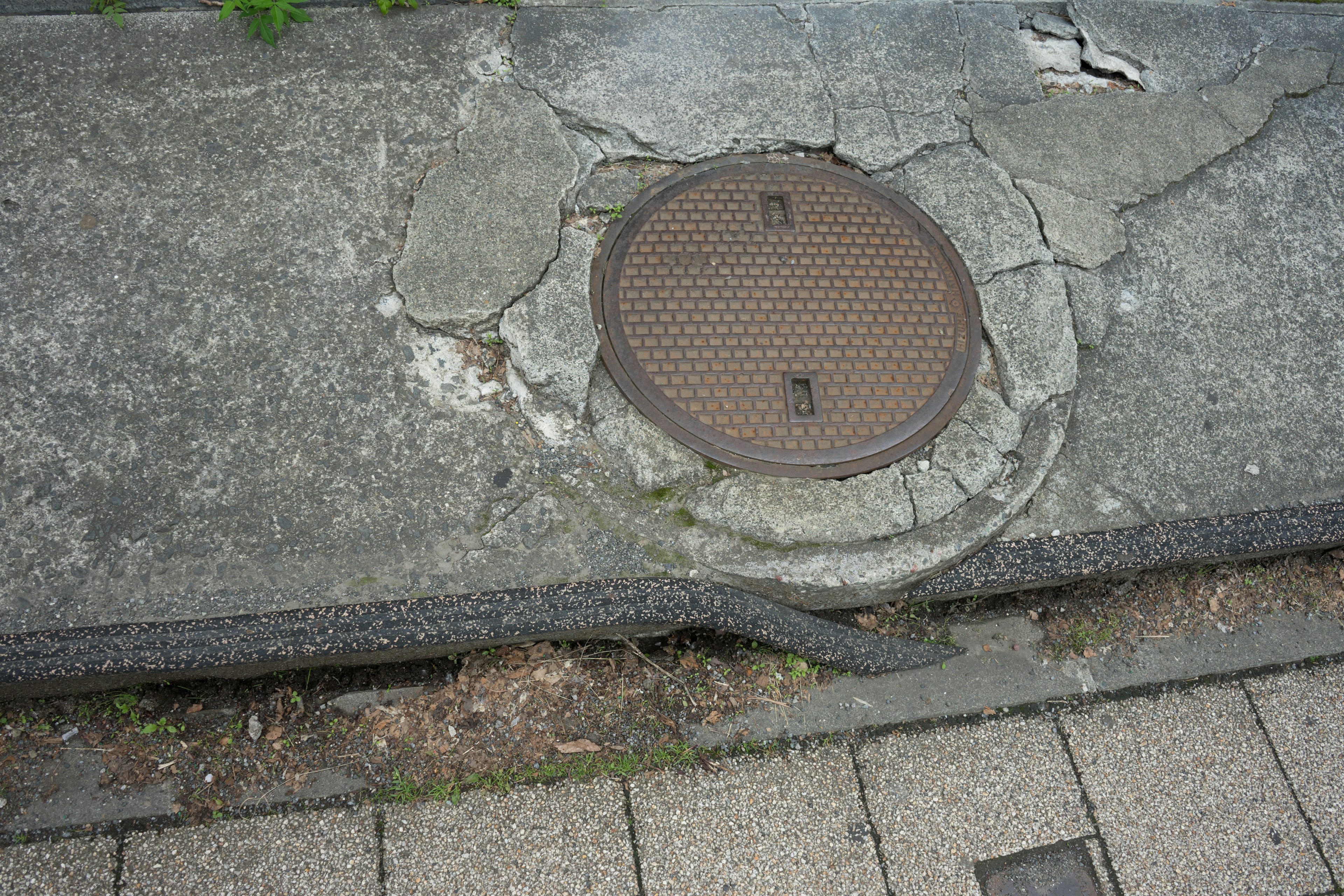 Acera de concreto agrietada con una tapa de alcantarilla de metal