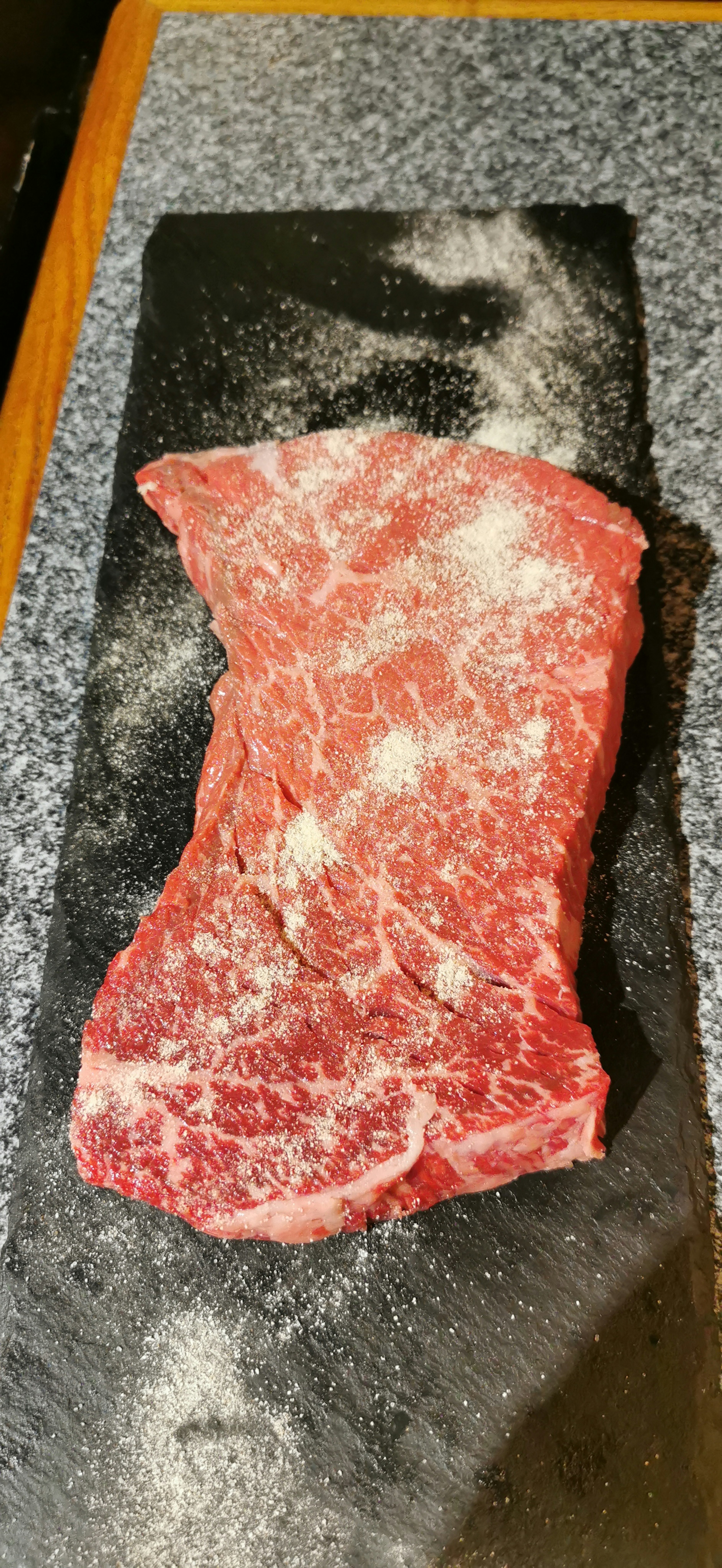 Raw red meat seasoned with flour on a black stone surface