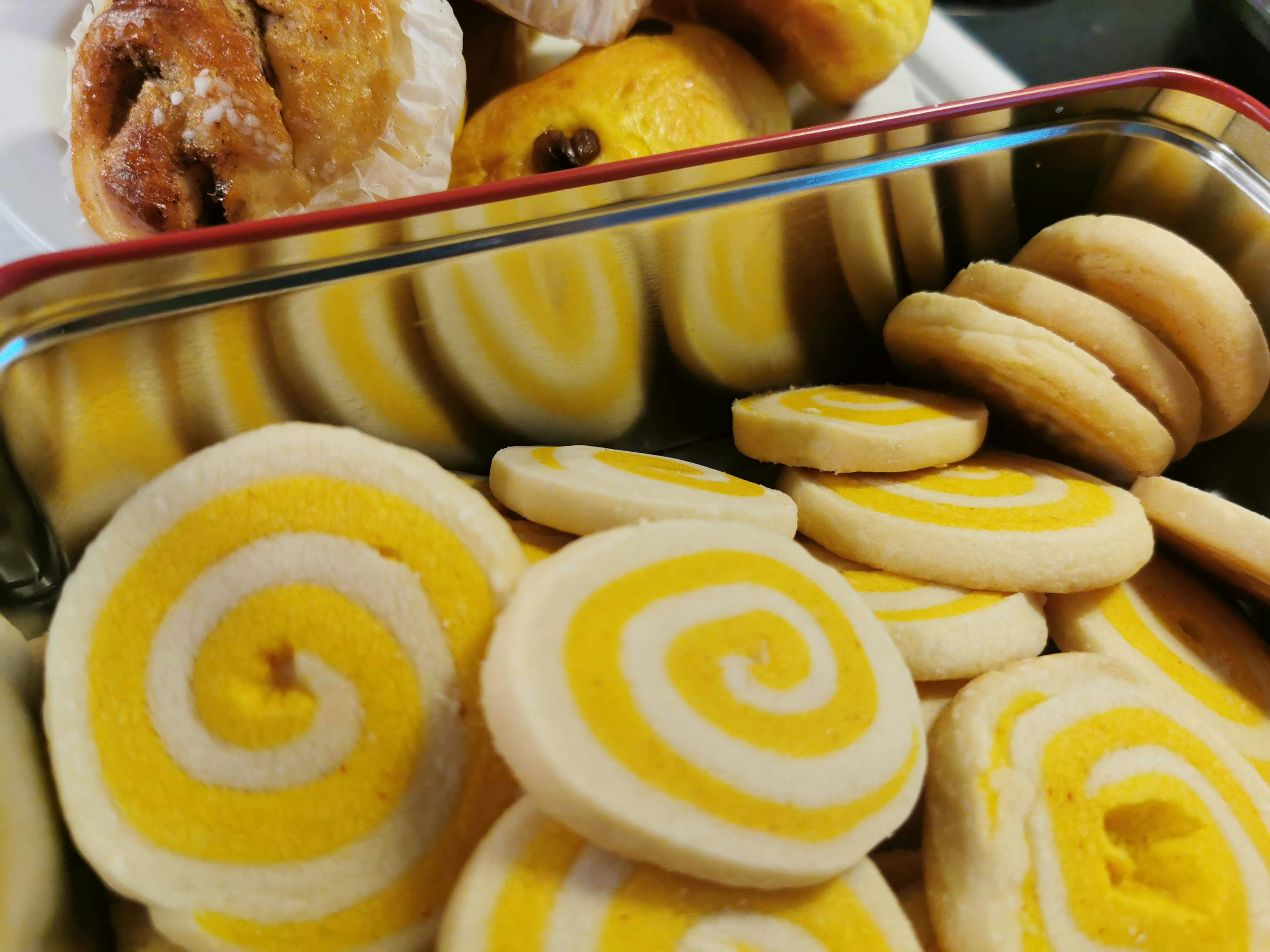 Container of yellow and white swirl cookies with baked goods in the background