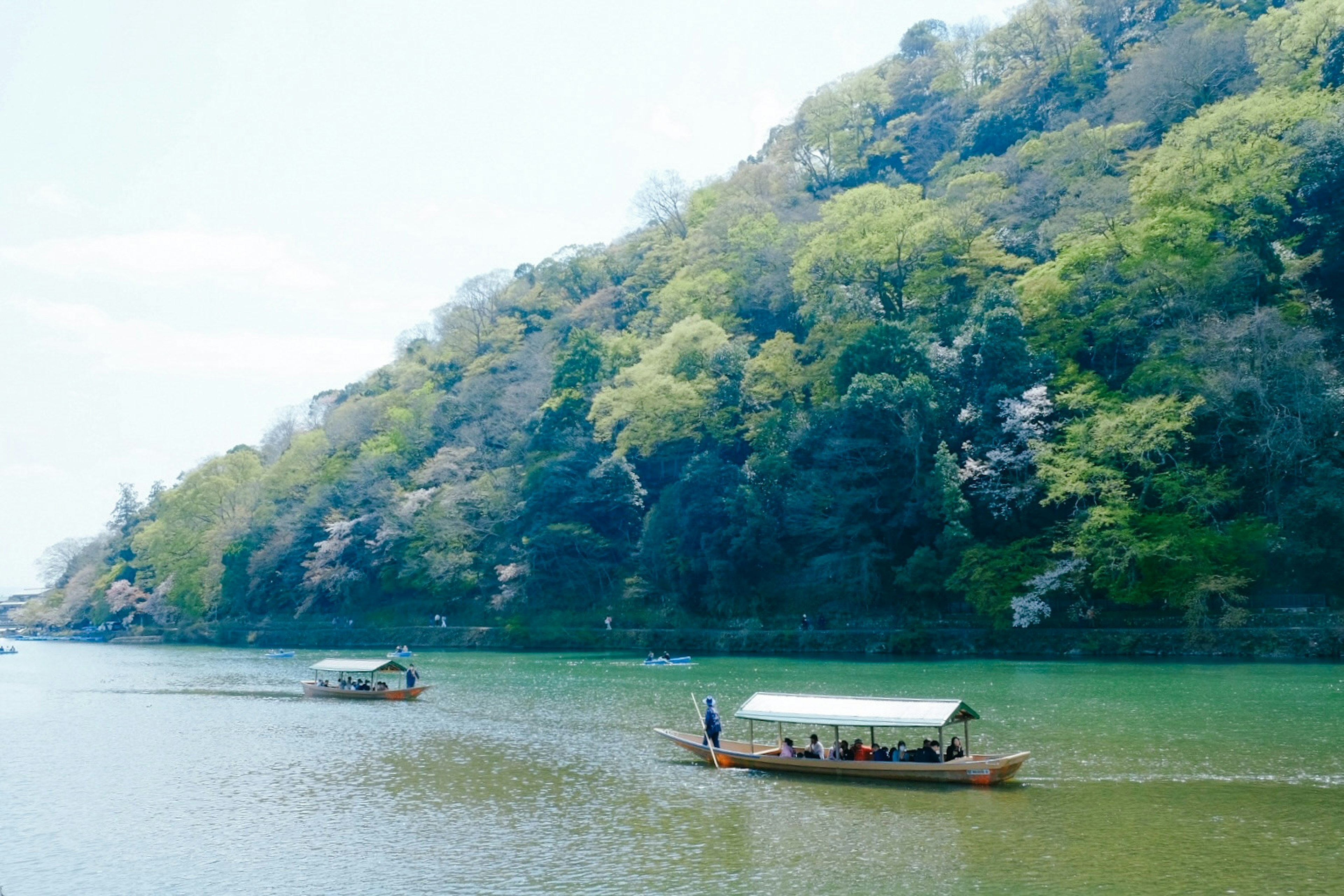 A tranquil river with boats gliding past lush green hills