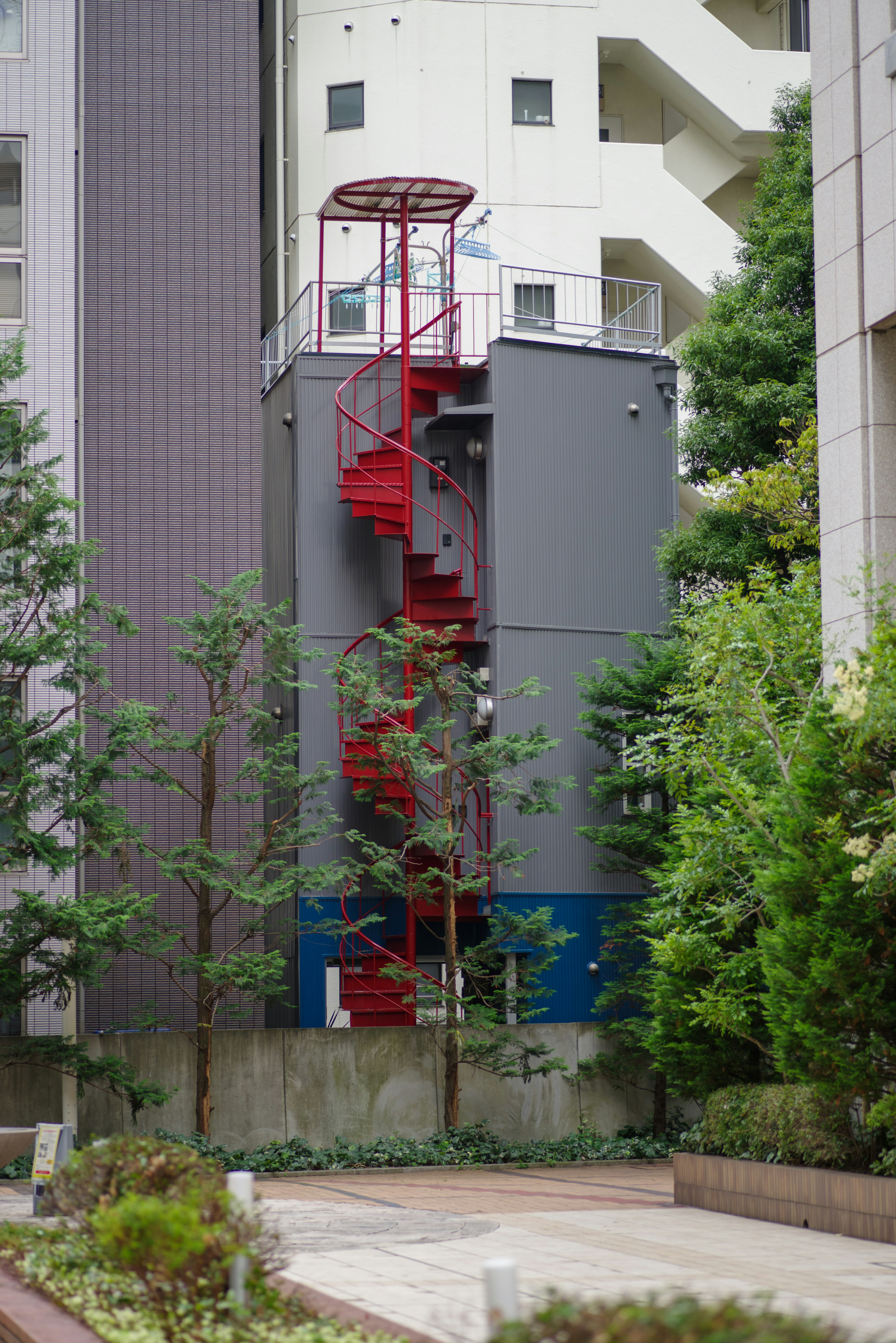 赤い螺旋階段が特徴的な灰色の建物と緑の木々