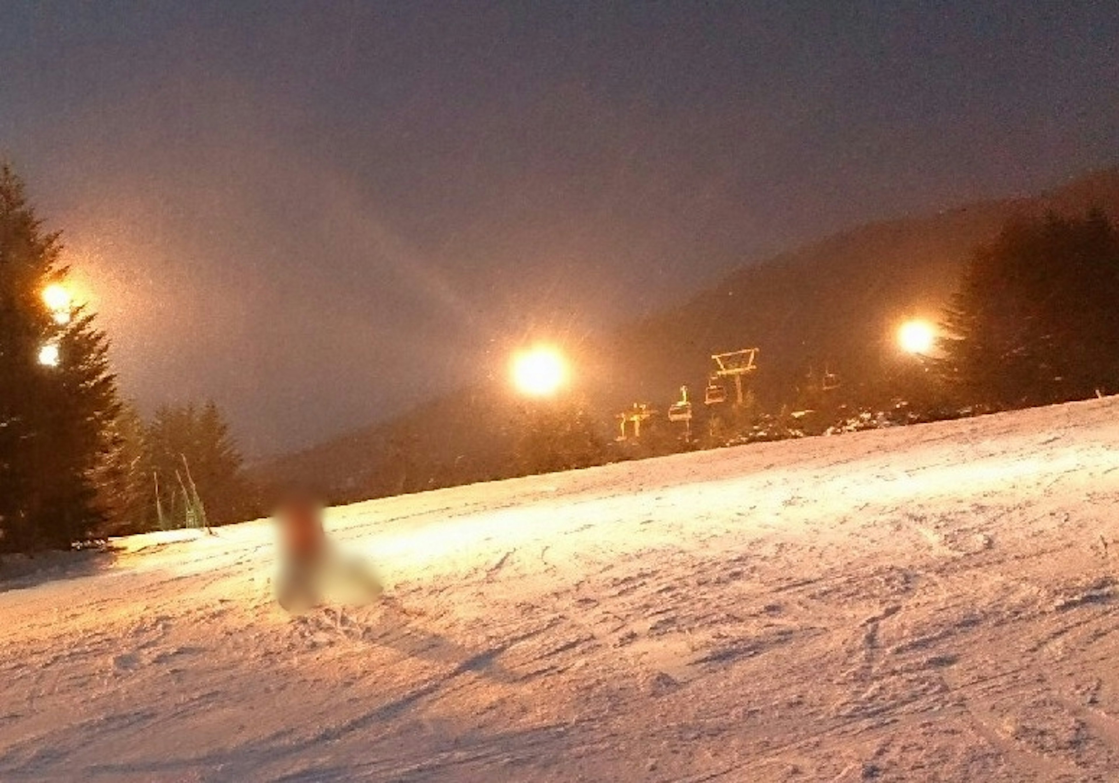 A person skiing on a snowy slope at night with lights