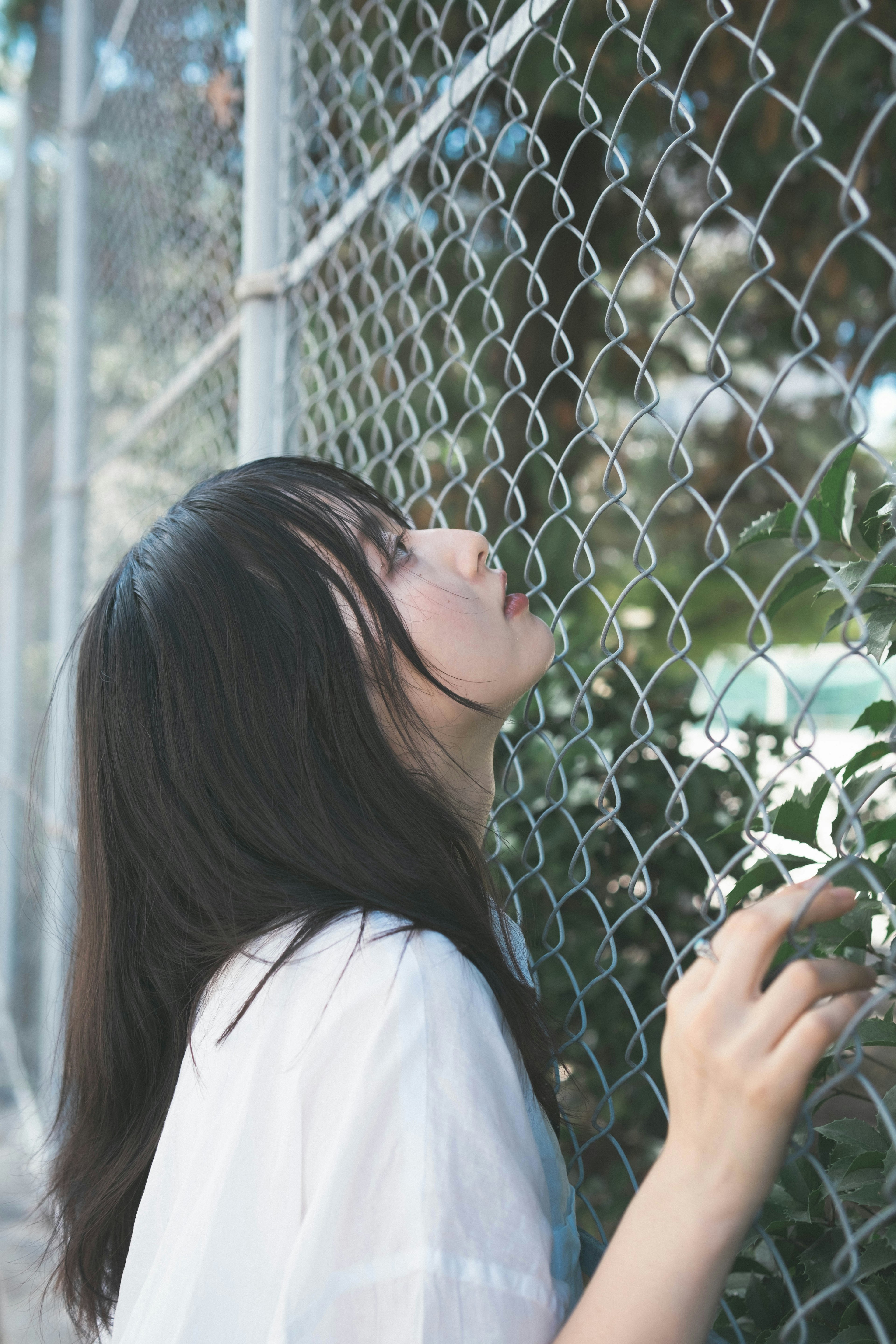 Side profile of a woman leaning against a chain-link fence