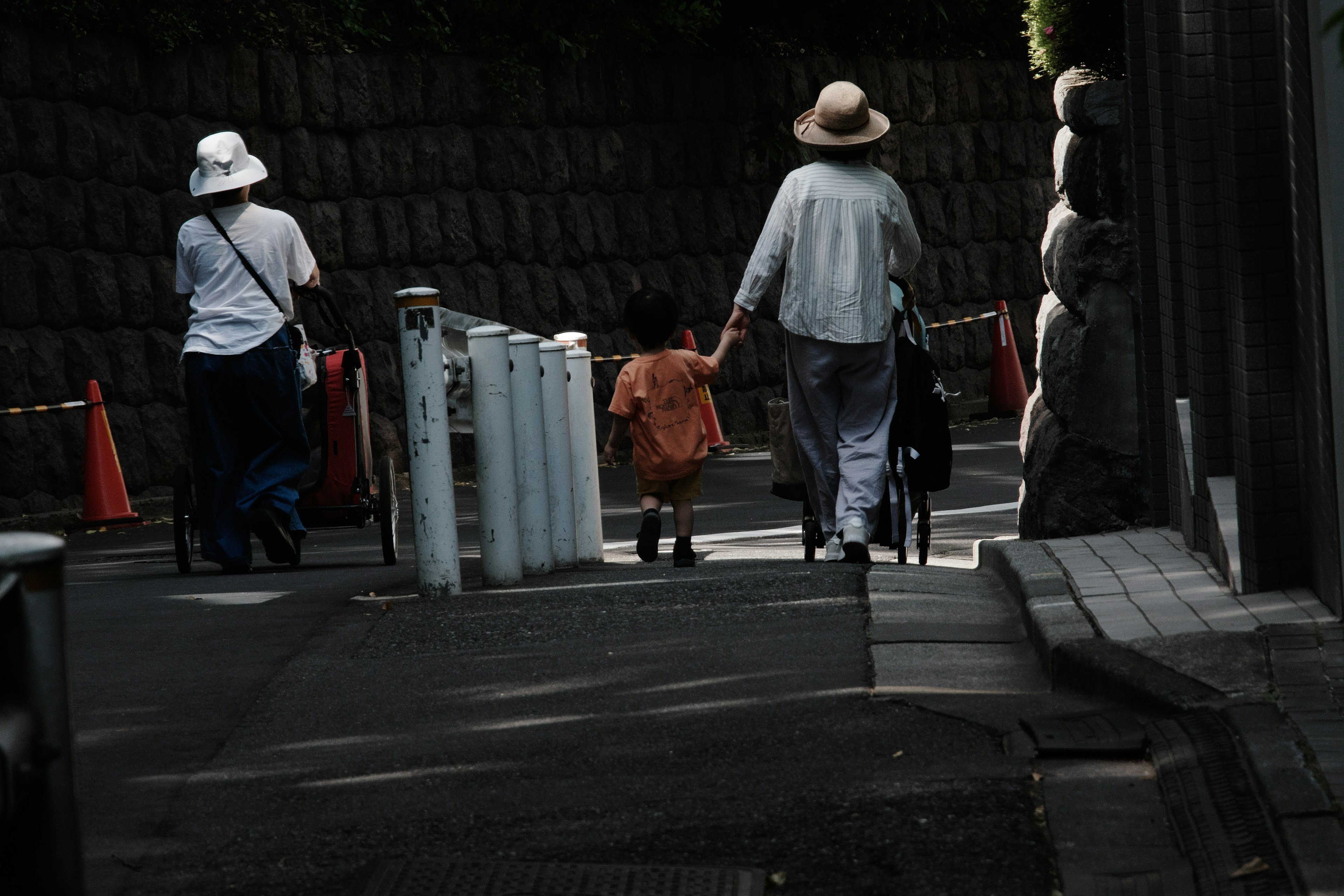 Adults and a child walking down a path, two adults wearing hats, child in orange clothing