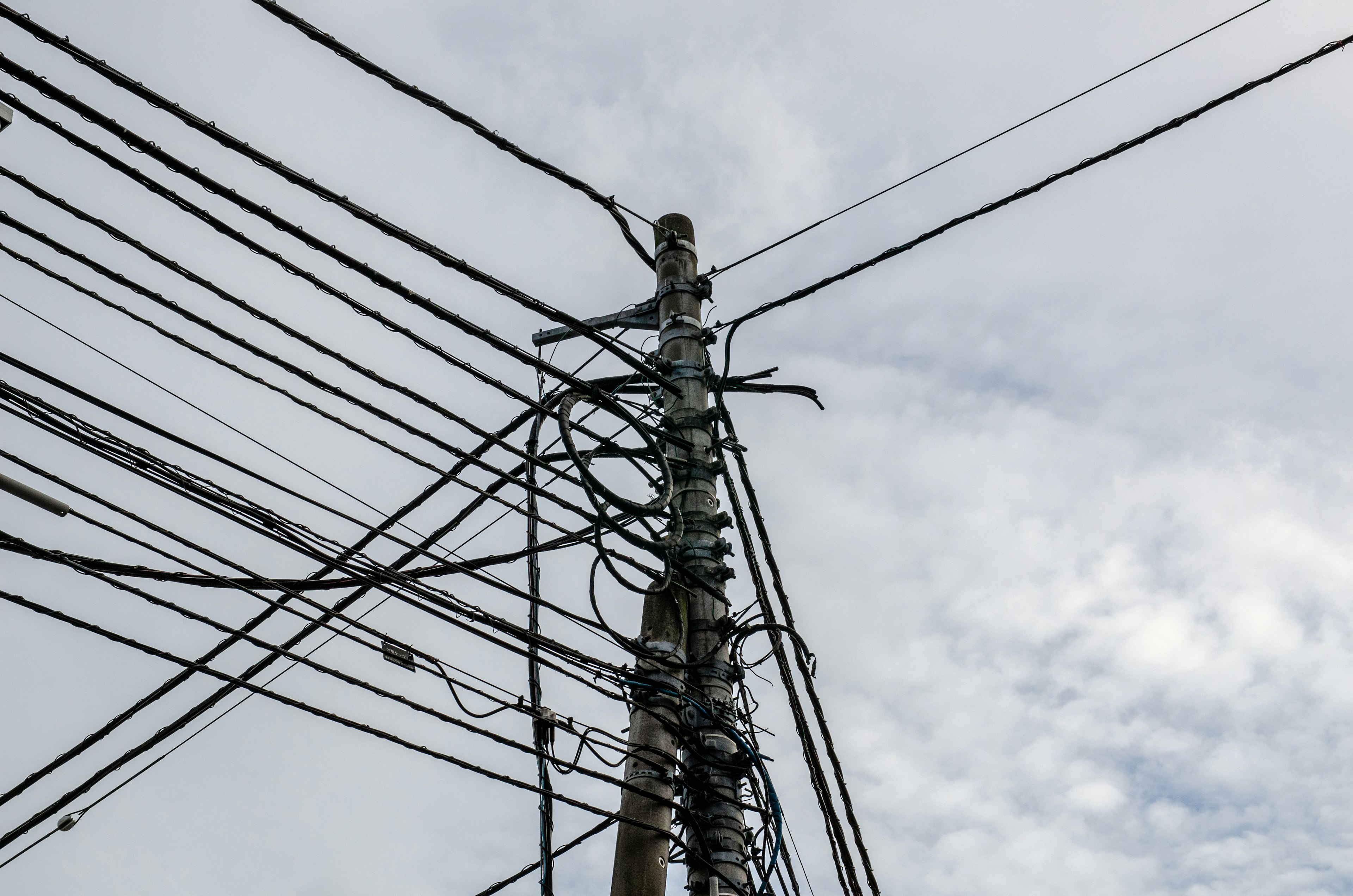 Utility pole with tangled power lines against a cloudy sky