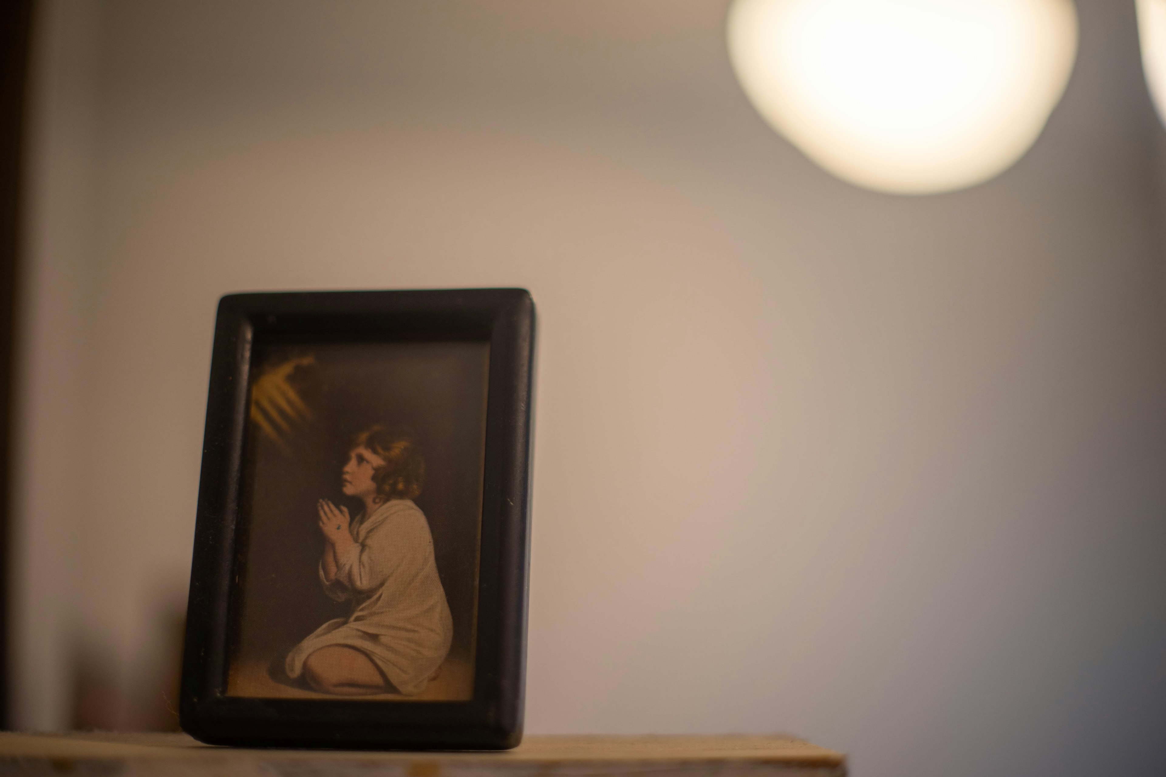 A black-framed photo of a child praying on a shelf