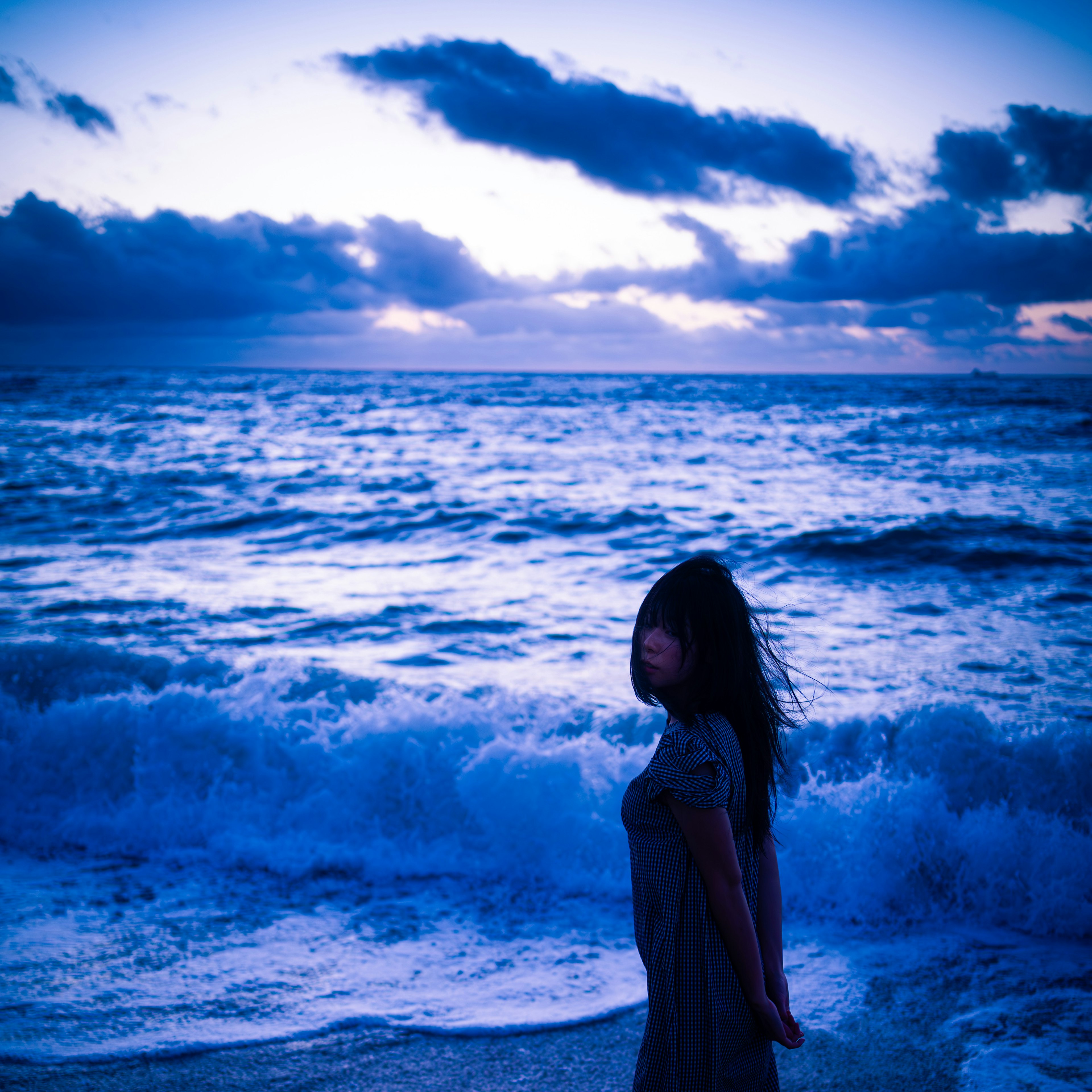 Silhouette einer Frau am Meer mit blauem Abendhimmel und Wellen