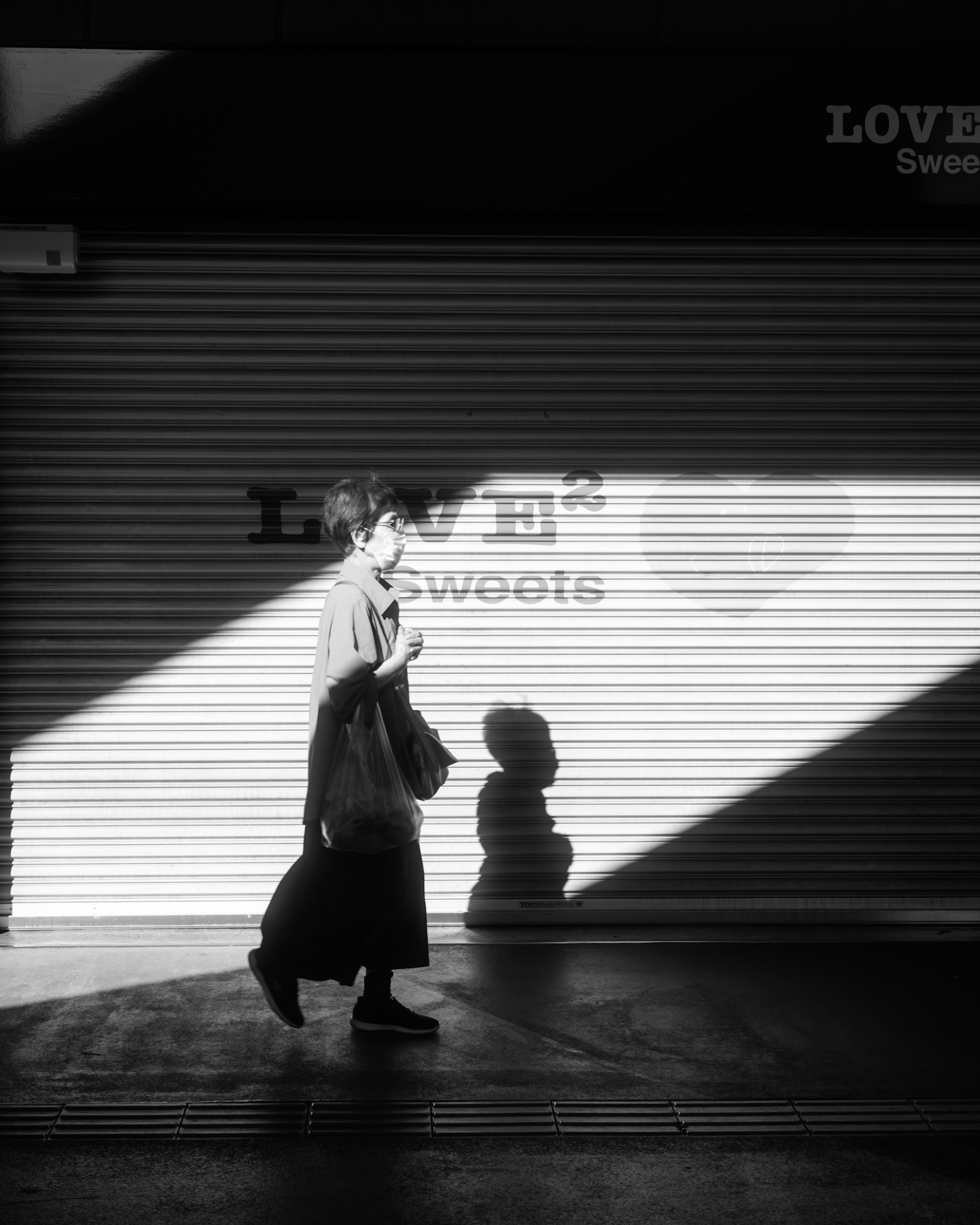 Una persona caminando en blanco y negro contra un fondo de luz y sombra