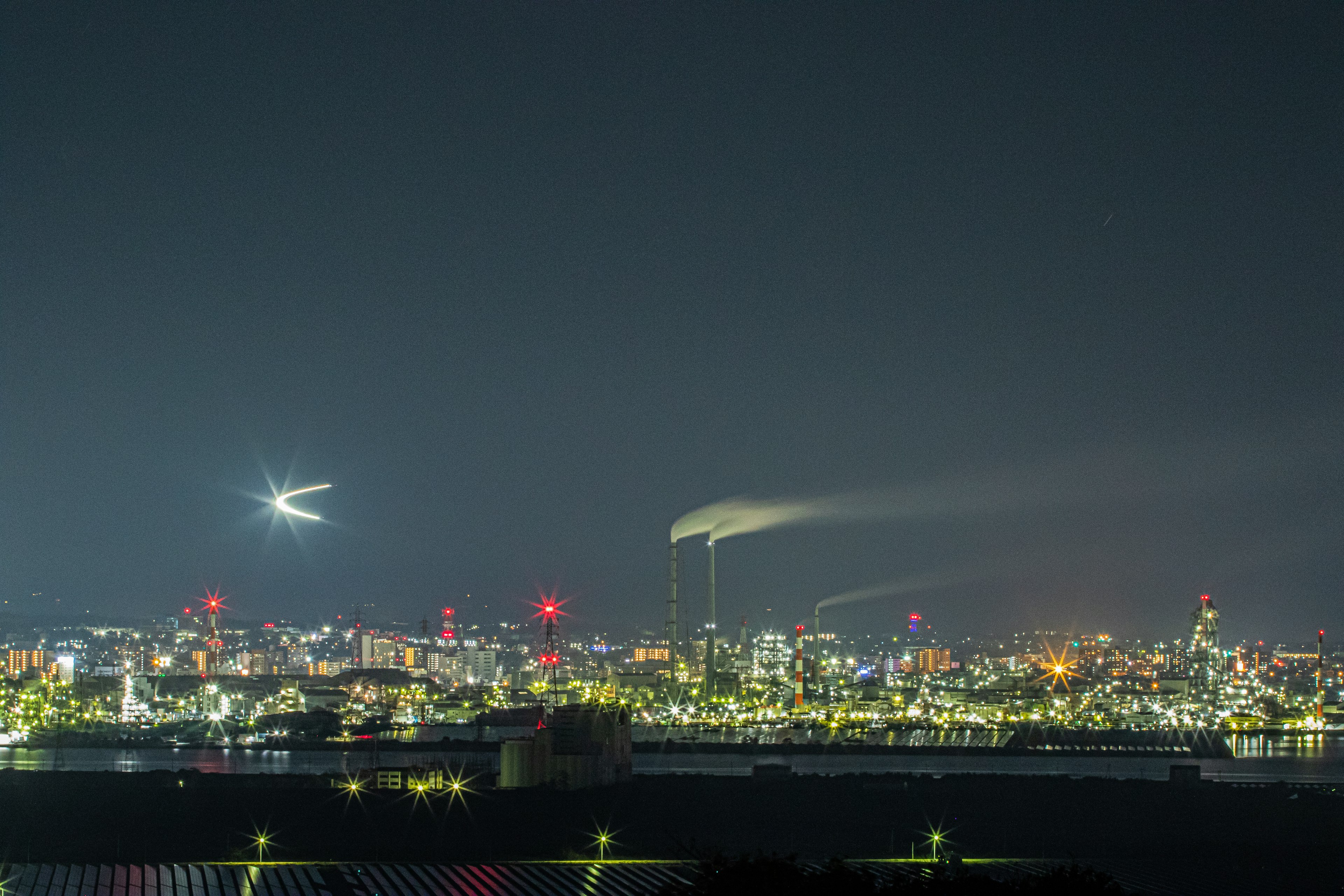 Nighttime cityscape featuring skyscrapers and smokestacks