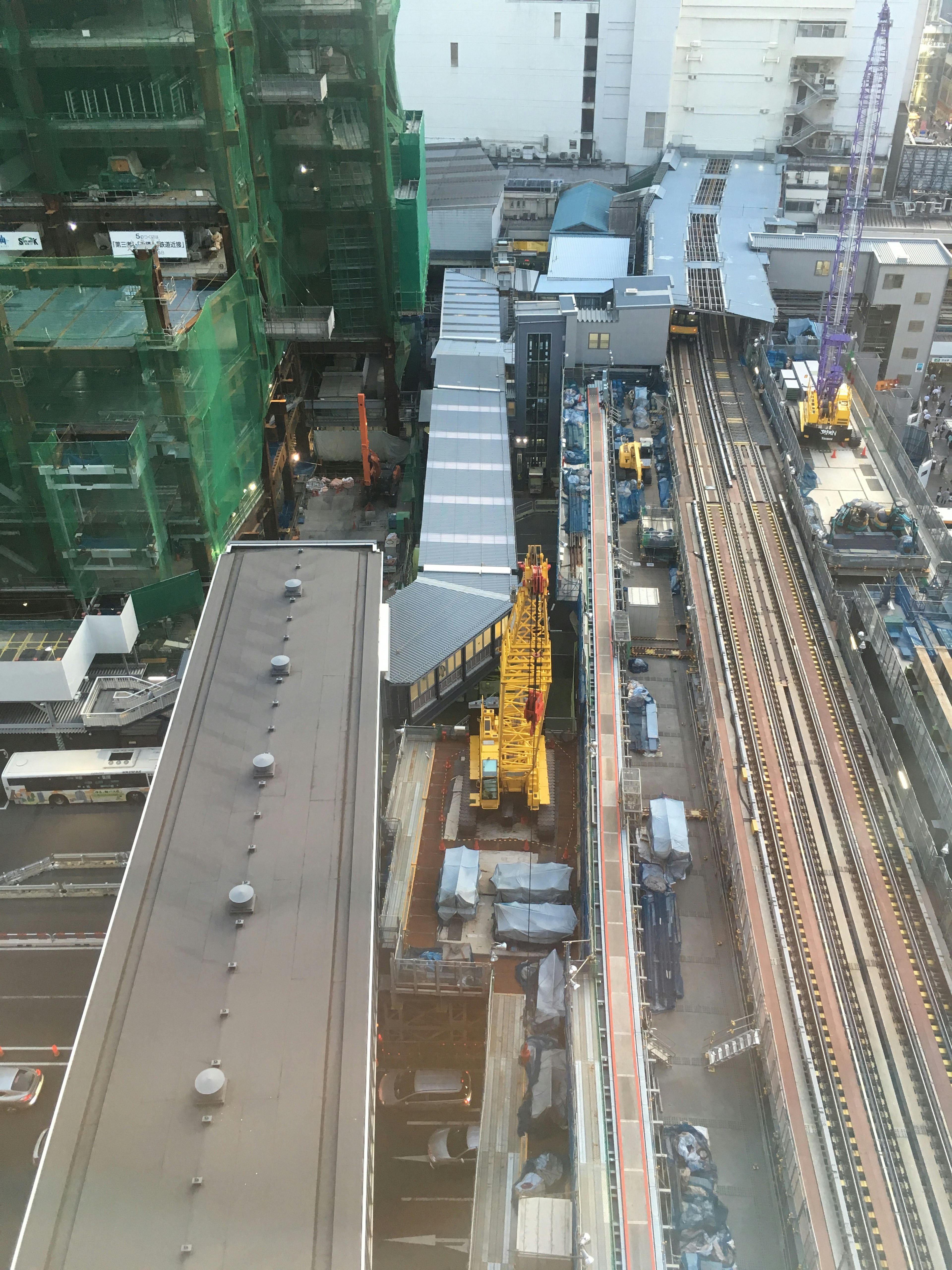 Aerial view of a construction site between high-rise buildings featuring a crane and railway tracks