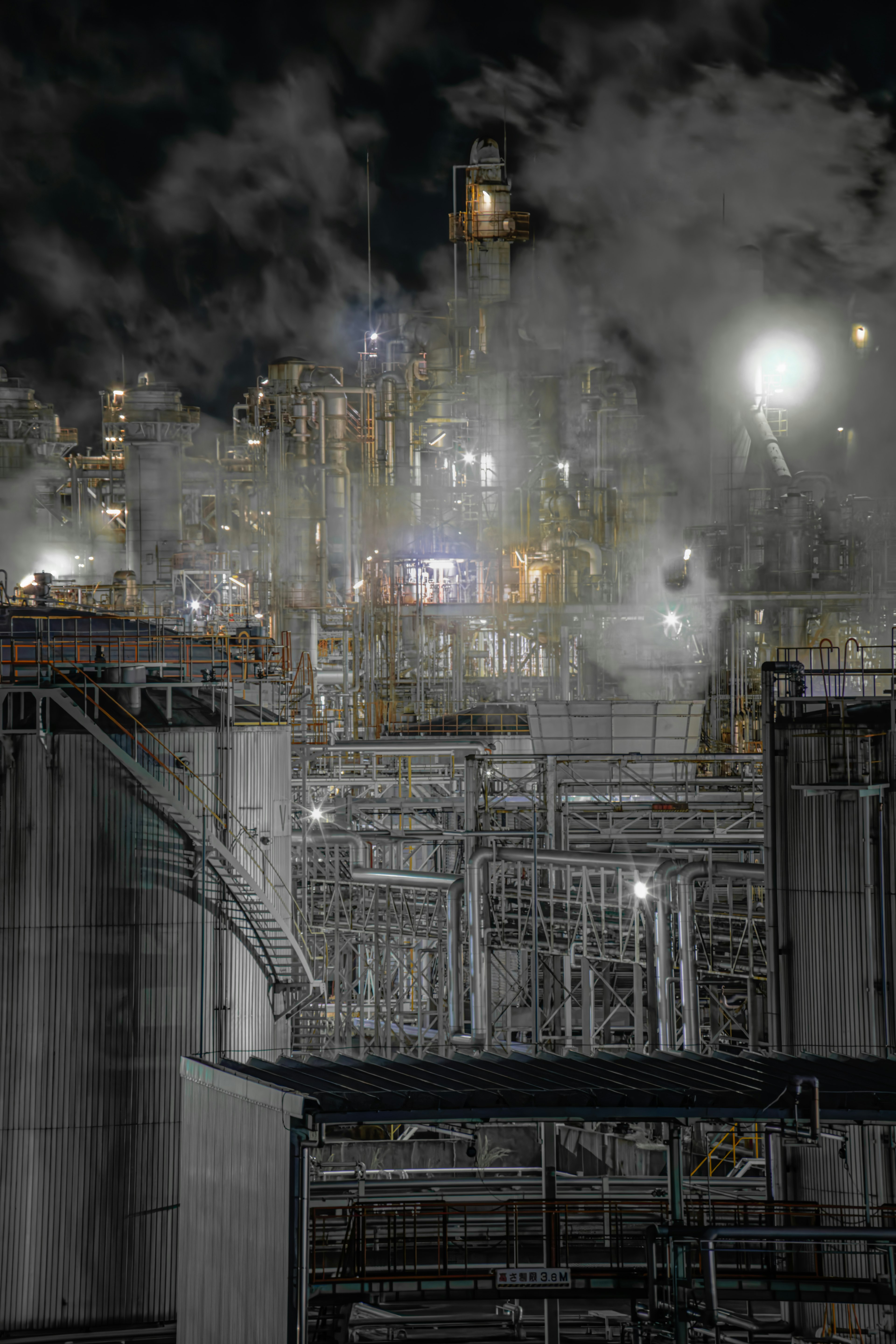 Vue nocturne d'une usine industrielle avec des tuyauteries complexes et de la vapeur