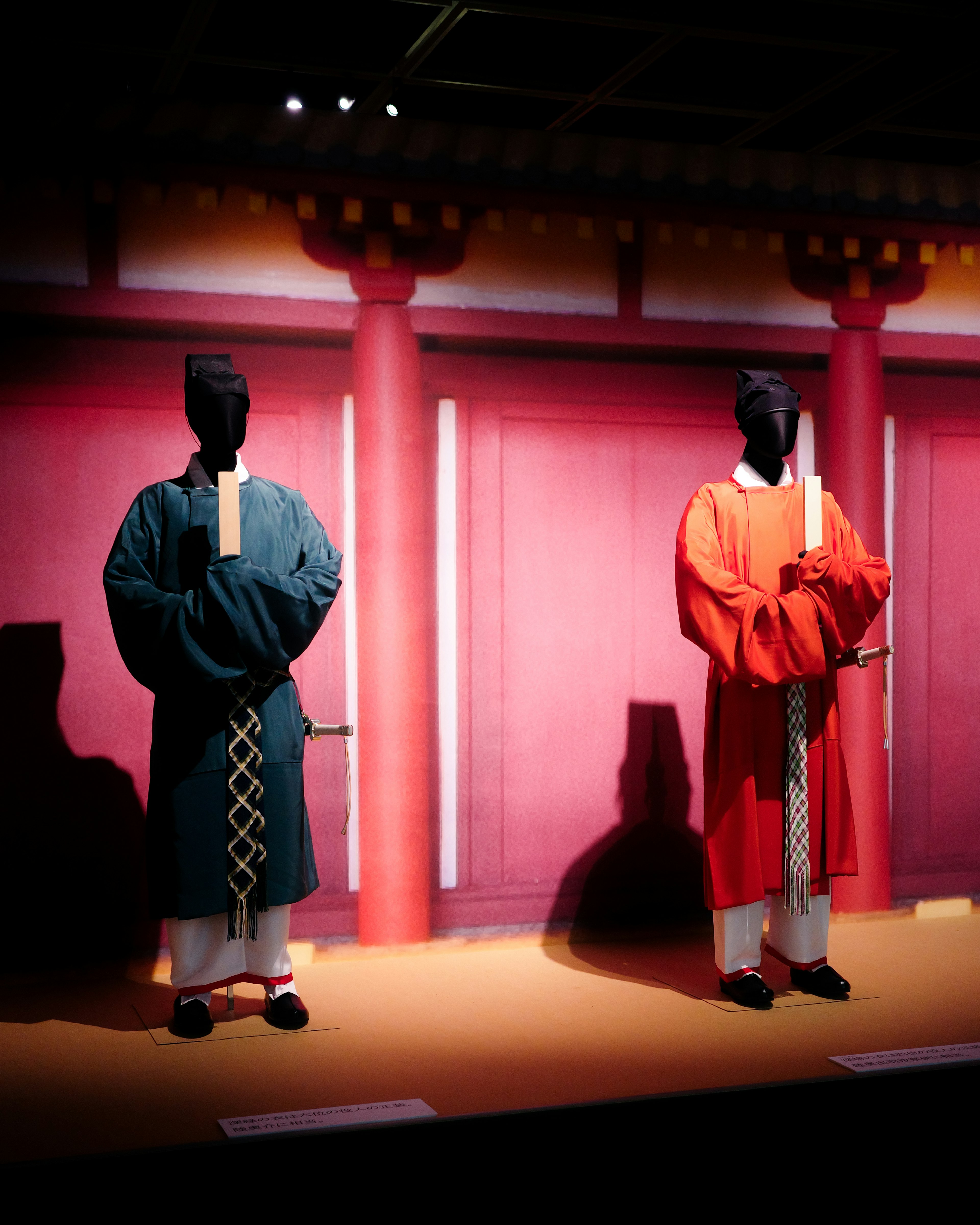 Two mannequins dressed in traditional blue and red garments with a colorful wall background