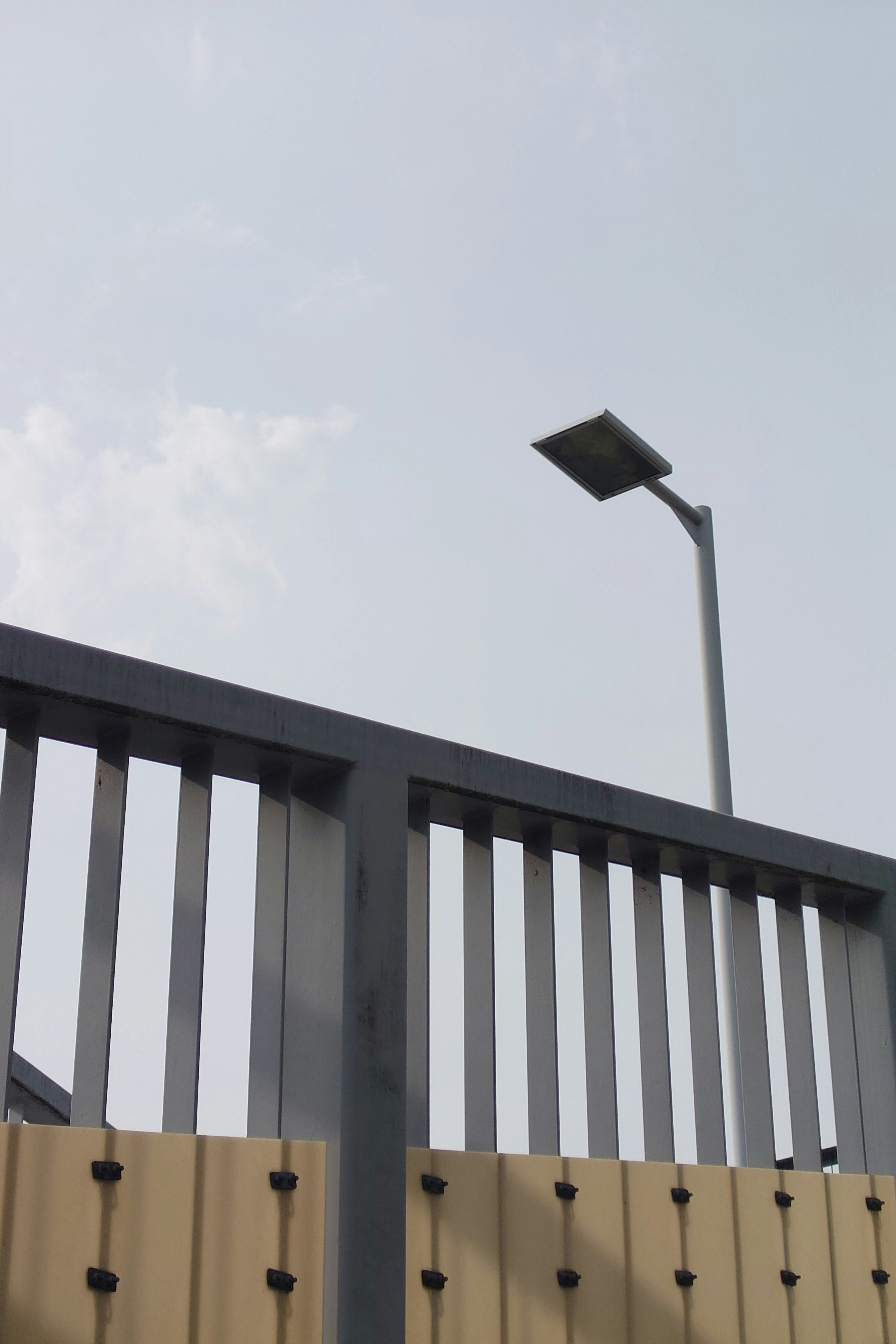 Valla de metal y farola en silueta contra un cielo azul