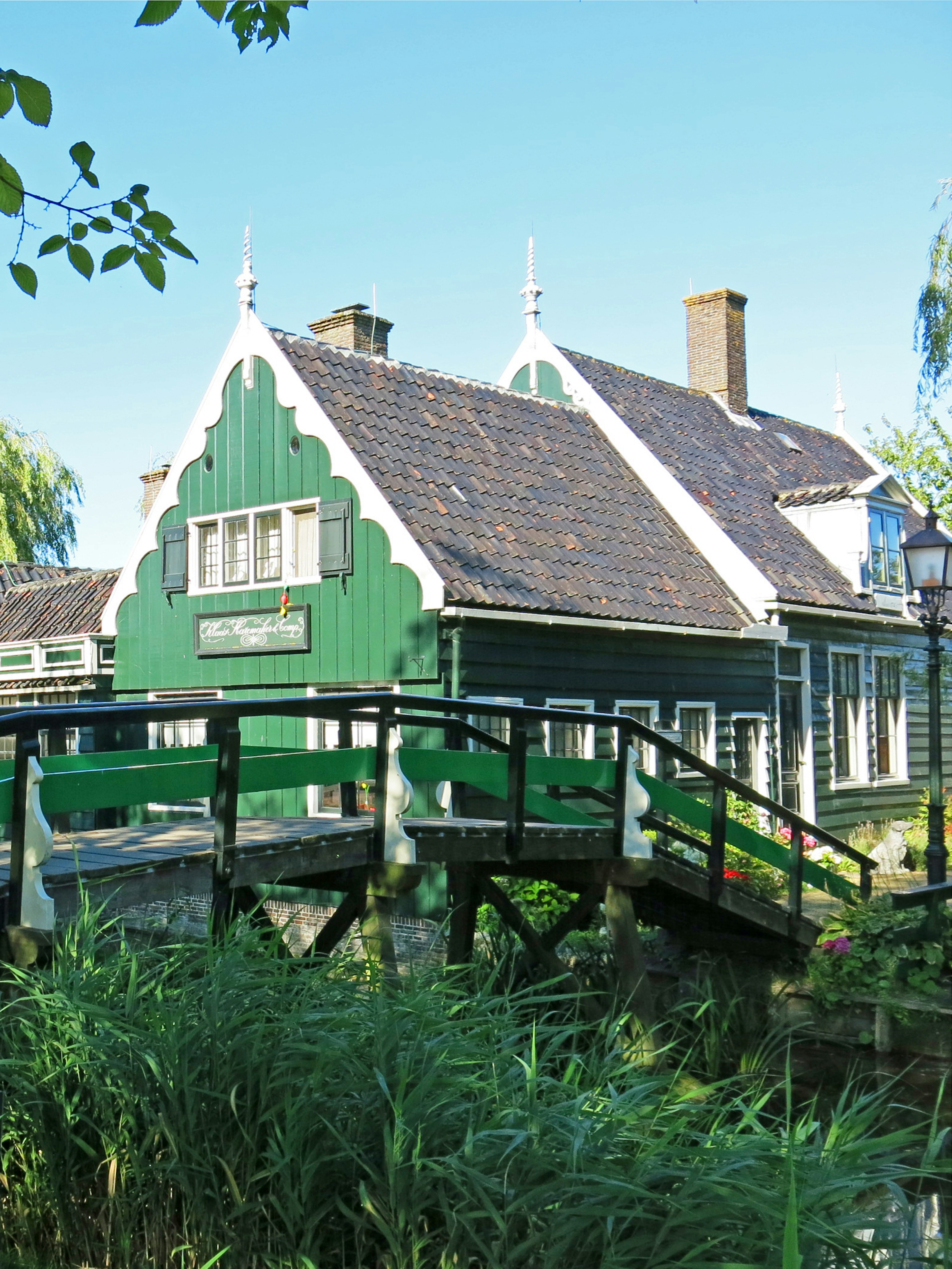 Traditional Dutch house with green exterior and distinctive roof near a small bridge