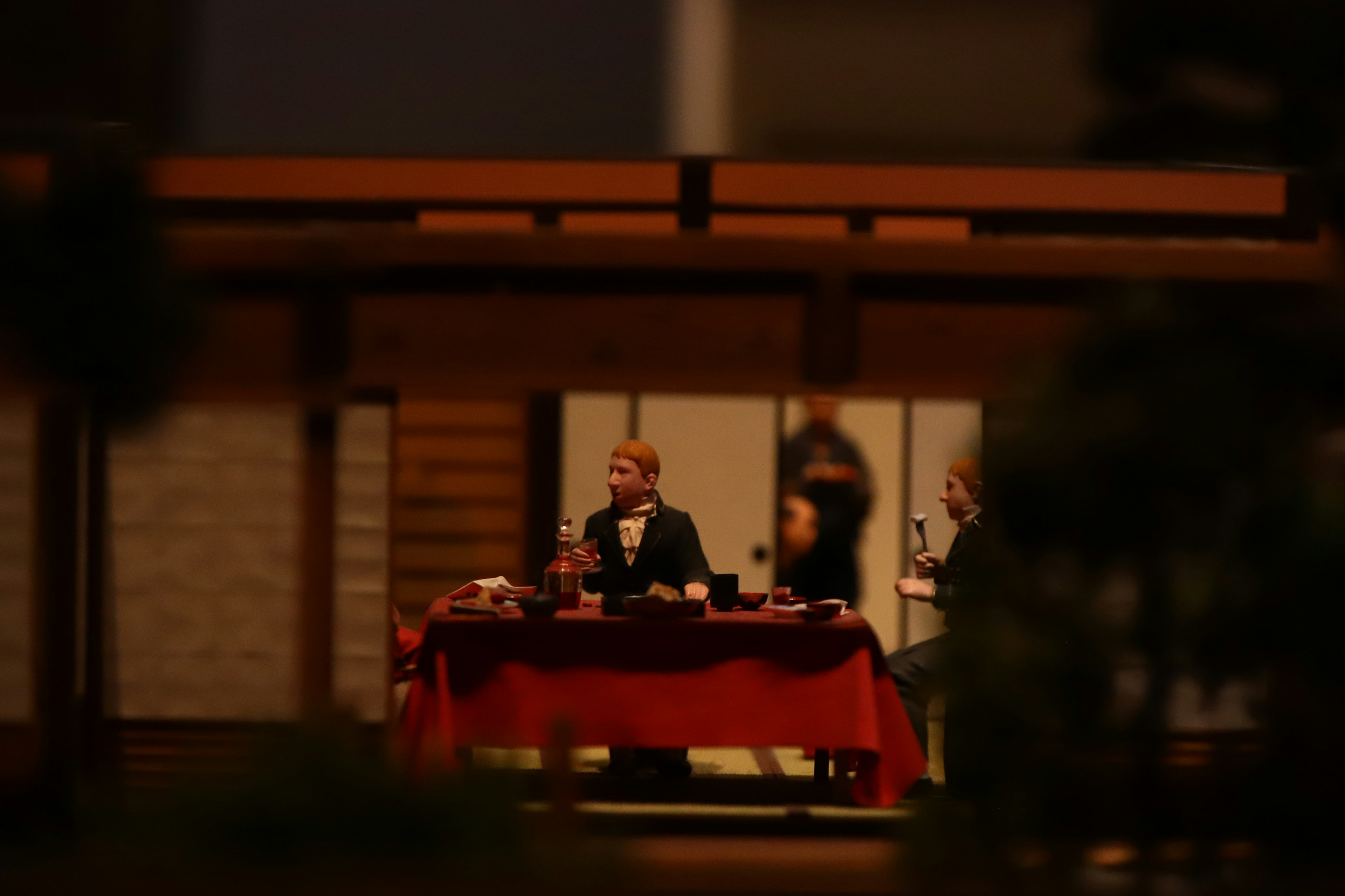 Escena en miniatura con dos figuras en una mesa cubierta con un mantel rojo