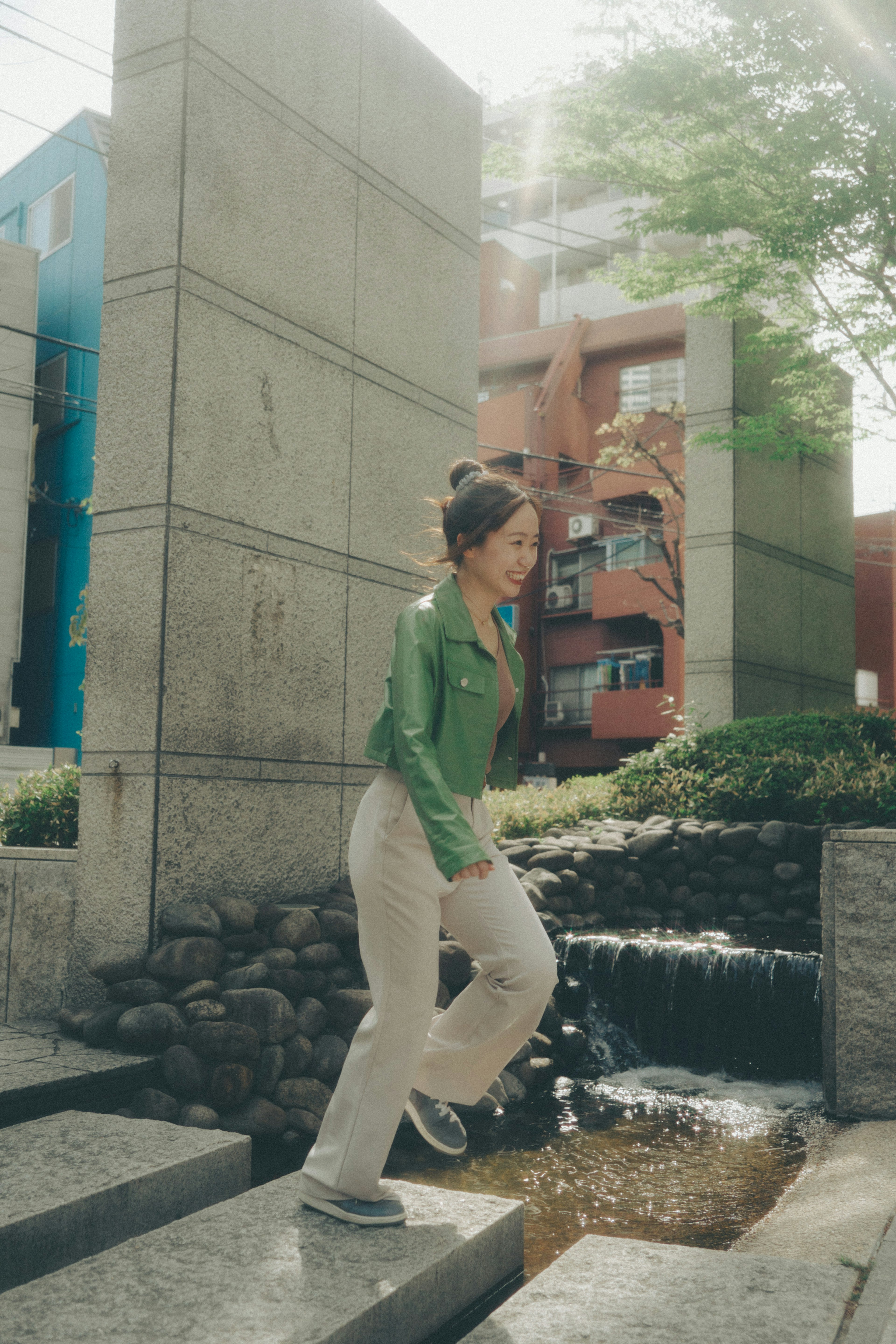 A woman in a green jacket walking near a flowing water feature