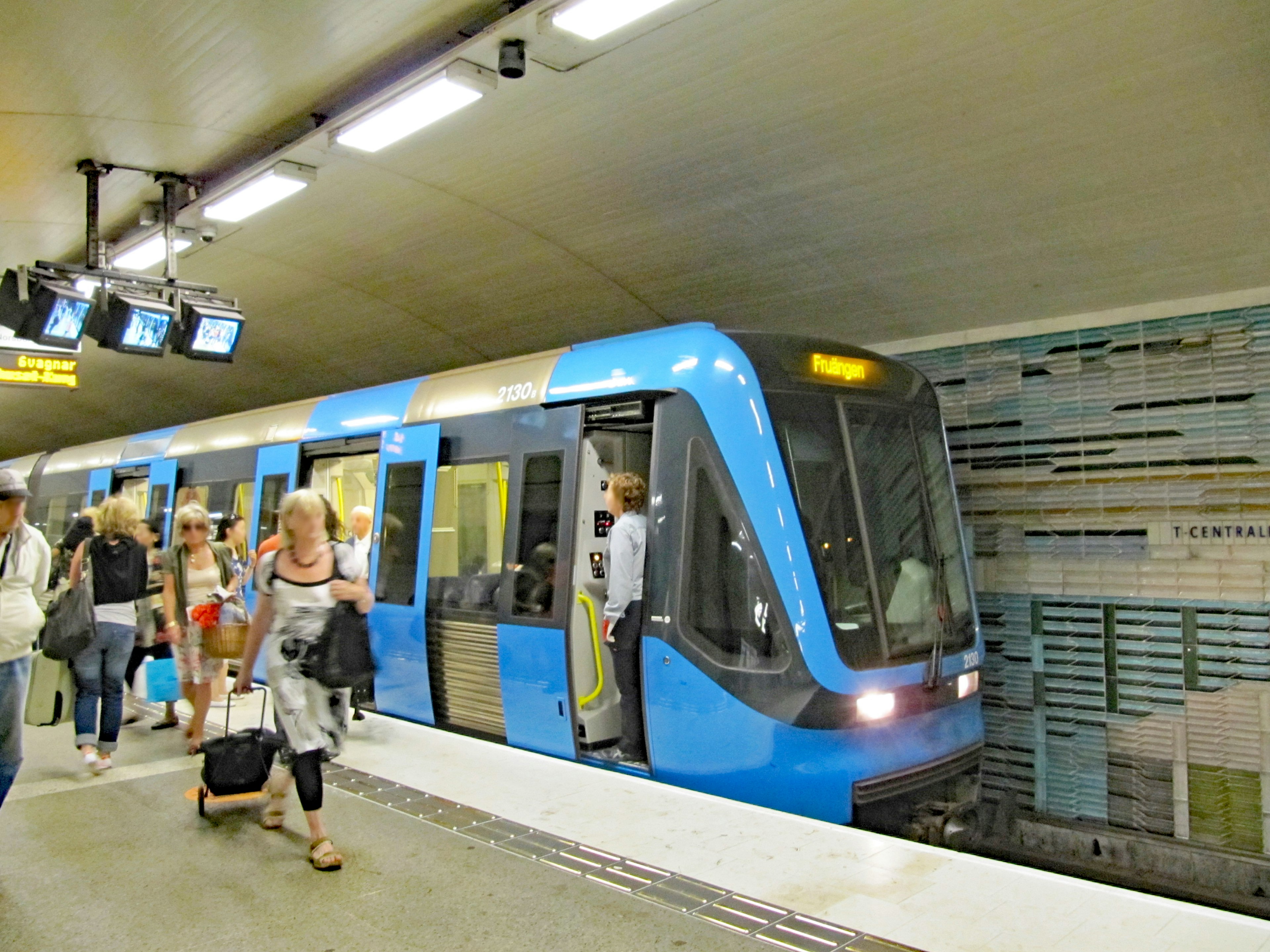 Tren de metro azul en una estación con pasajeros bajando