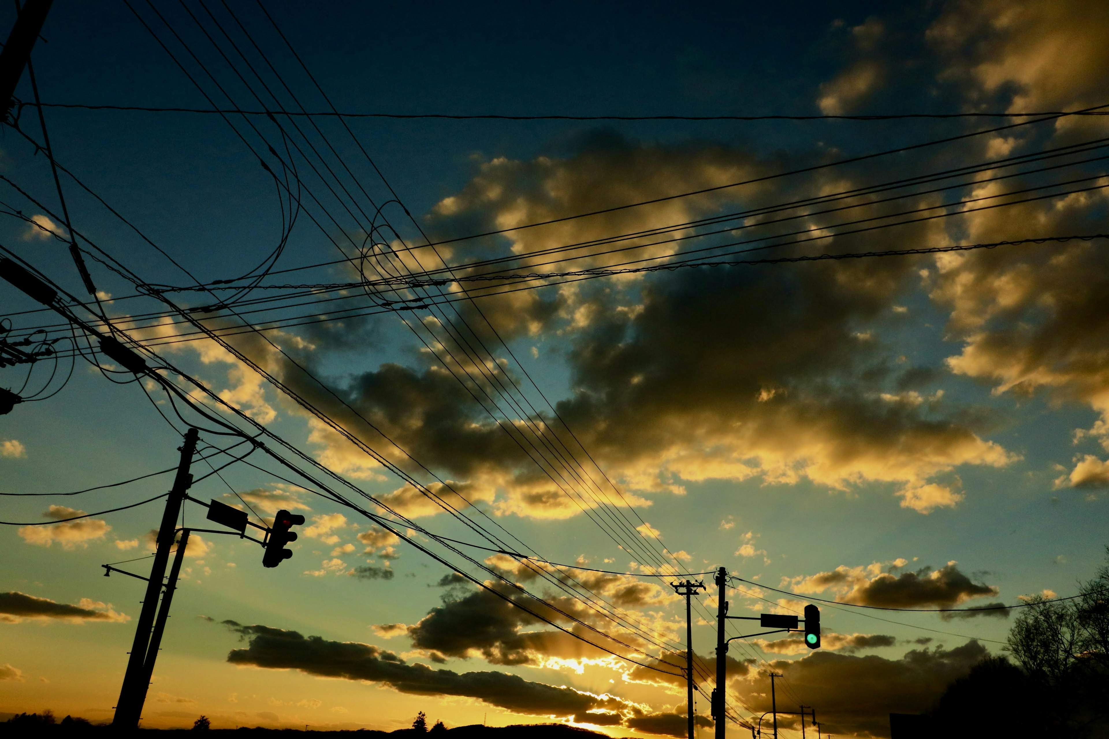 City intersection scene with sunset and dramatic clouds featuring power lines and traffic lights