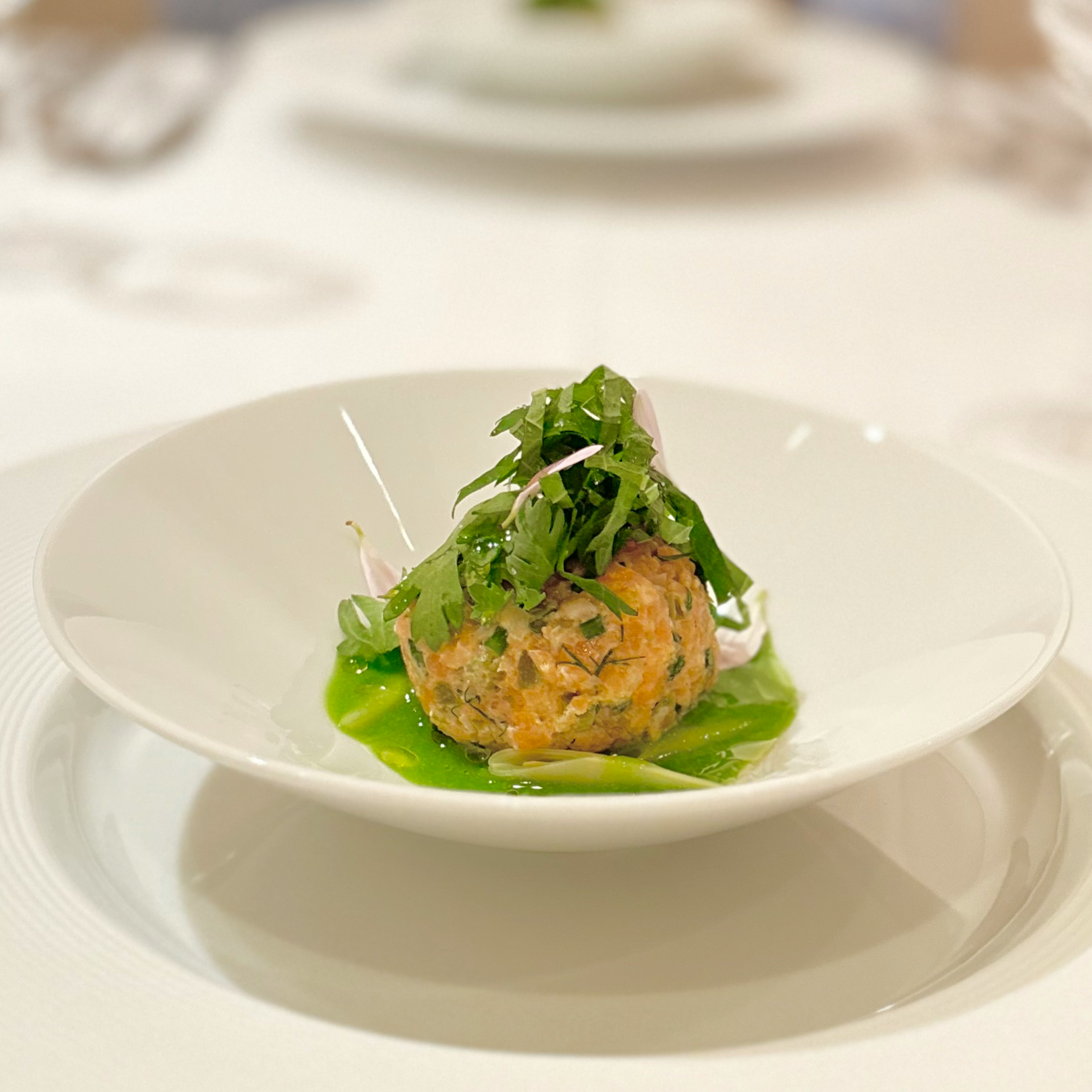 Un plato bellamente presentado con una albóndiga cubierta de hierbas y verduras sobre una salsa verde