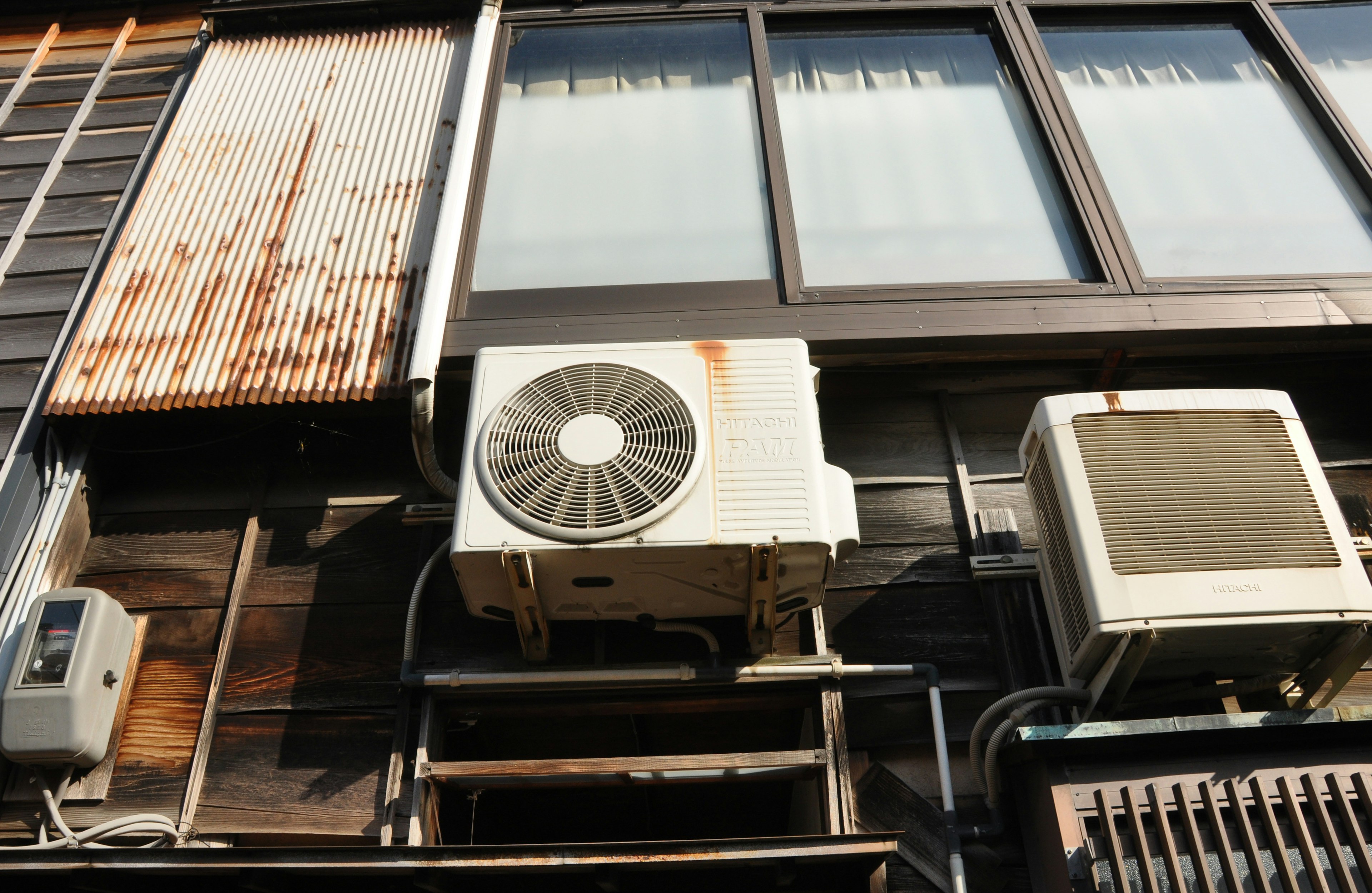 Air conditioning units mounted on the exterior wall of an old building with rusted metal panels