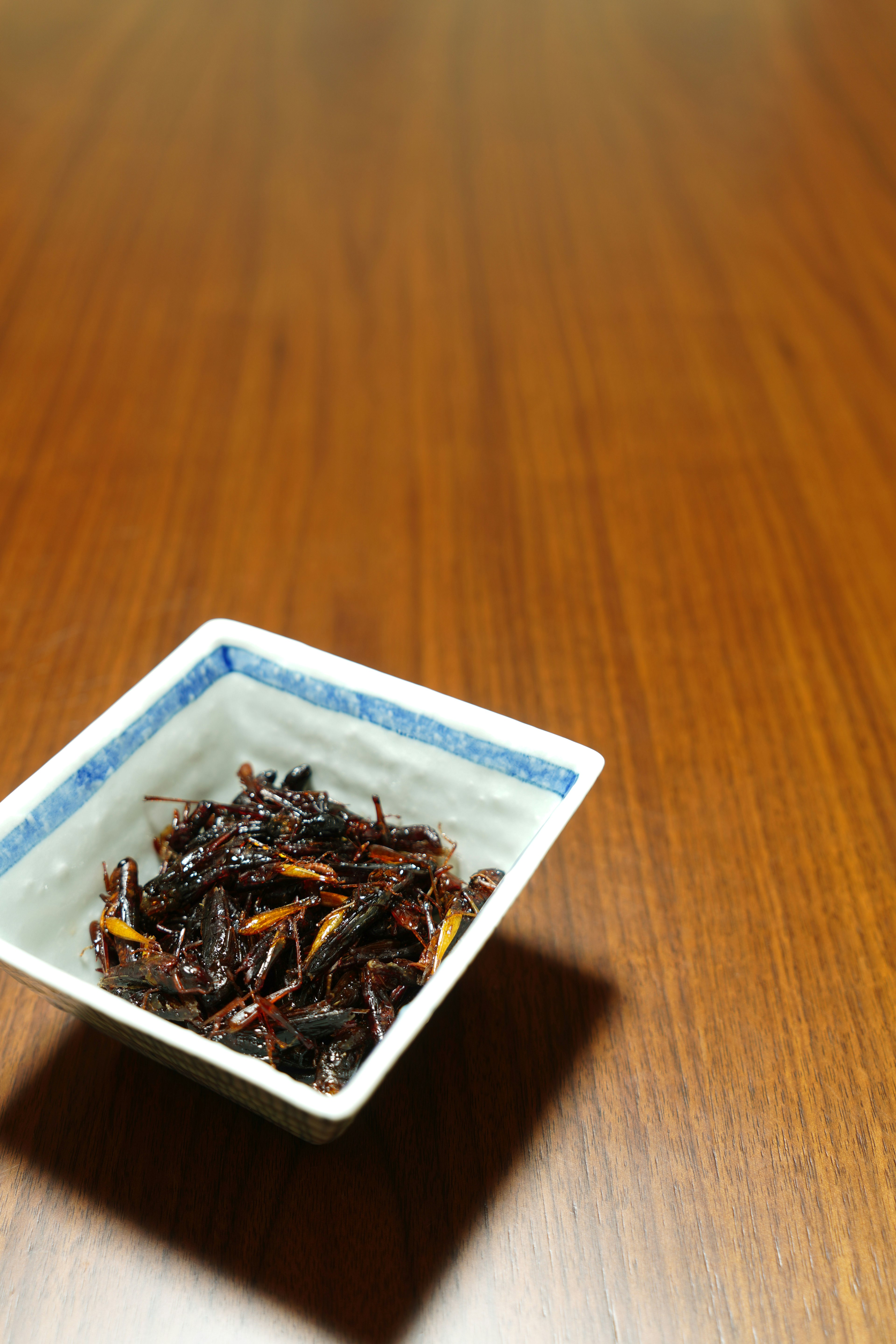 茶色のテーブルの上にある青い縁の小皿に盛られた乾燥した海藻