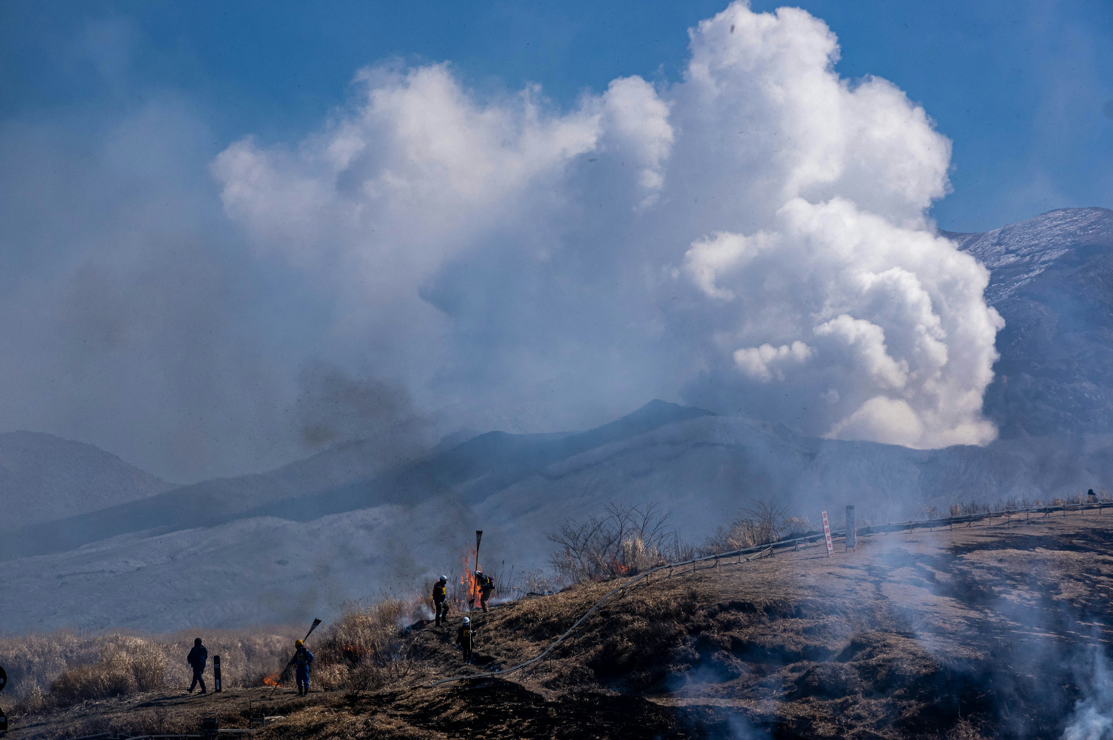 Orang-orang mendaki gunung dengan asap vulkanik di latar belakang