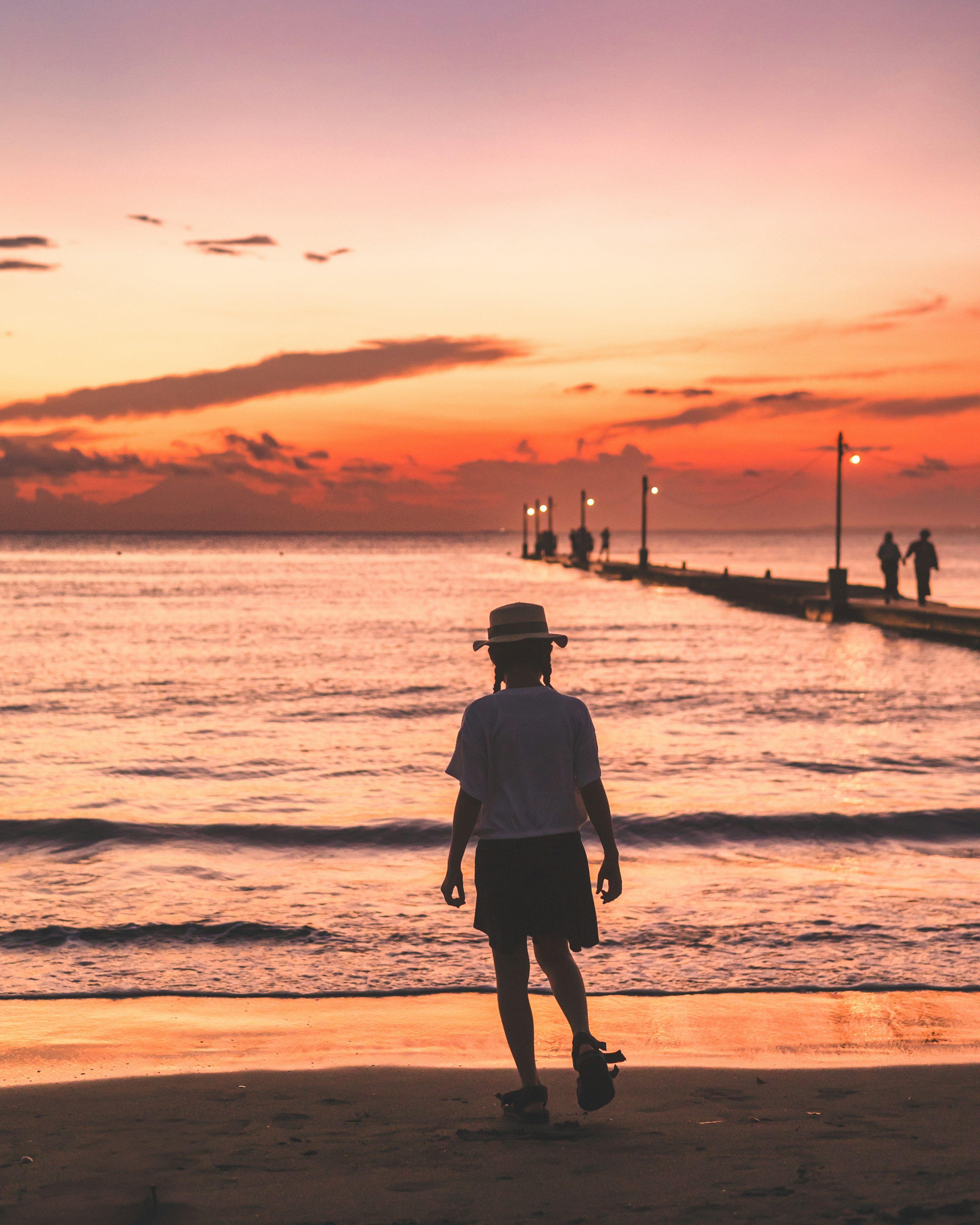 Un ragazzo che cammina sulla spiaggia al tramonto con un molo sullo sfondo