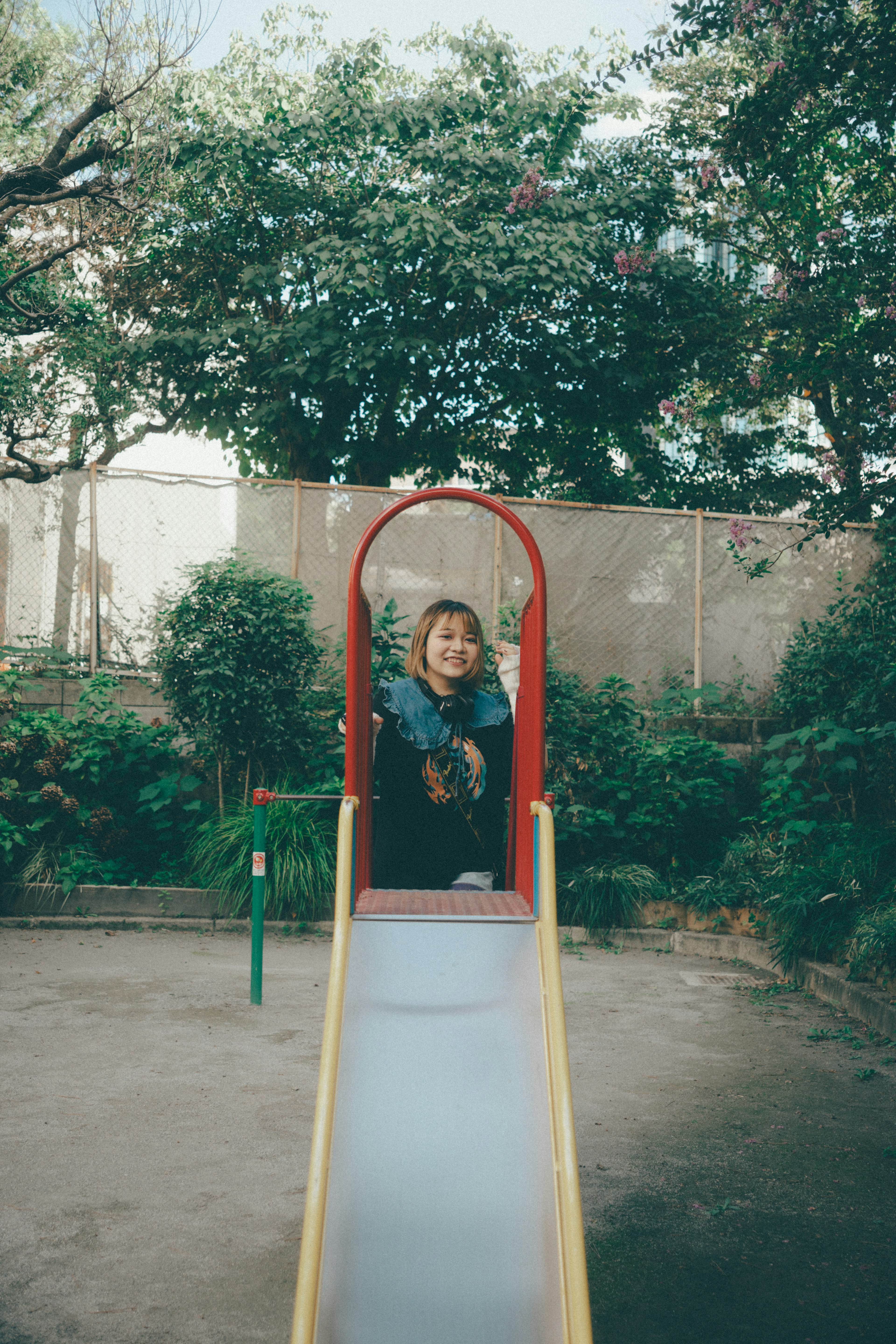 Child smiling on a playground slide with green foliage in the background