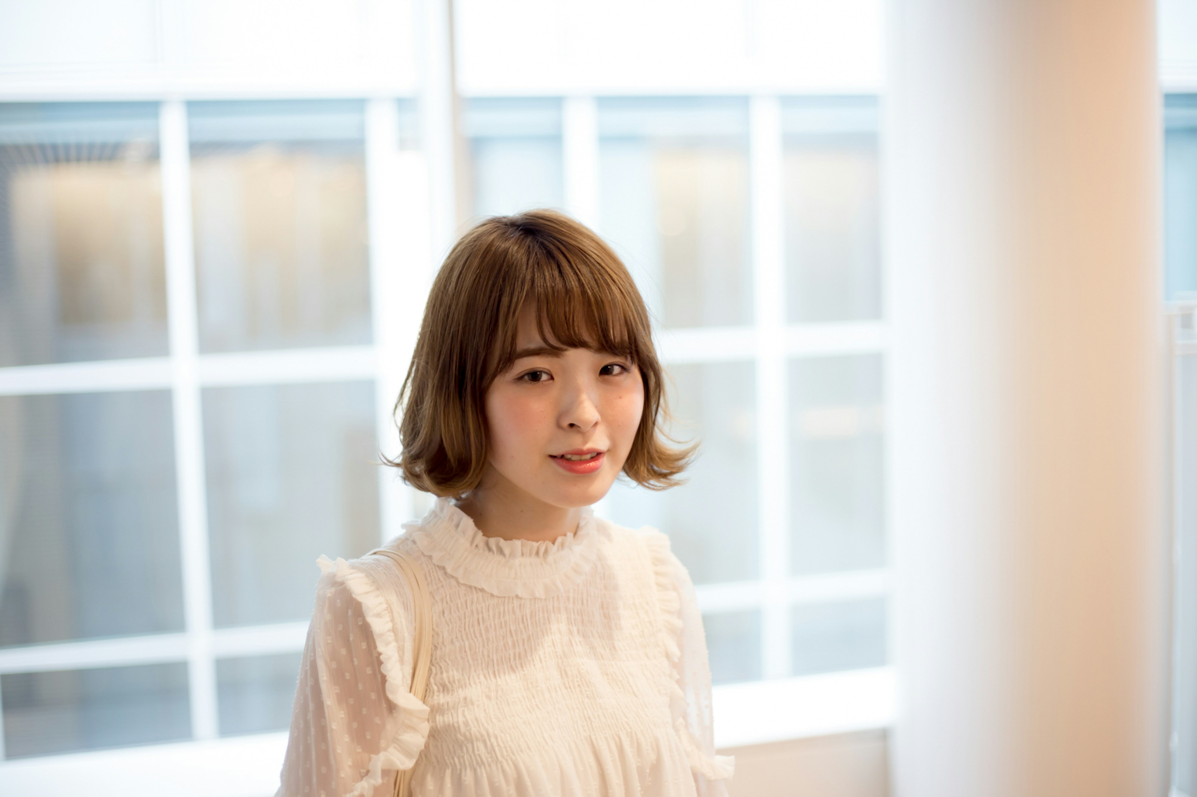 A woman with brown bob hair standing in front of a window wearing a white blouse