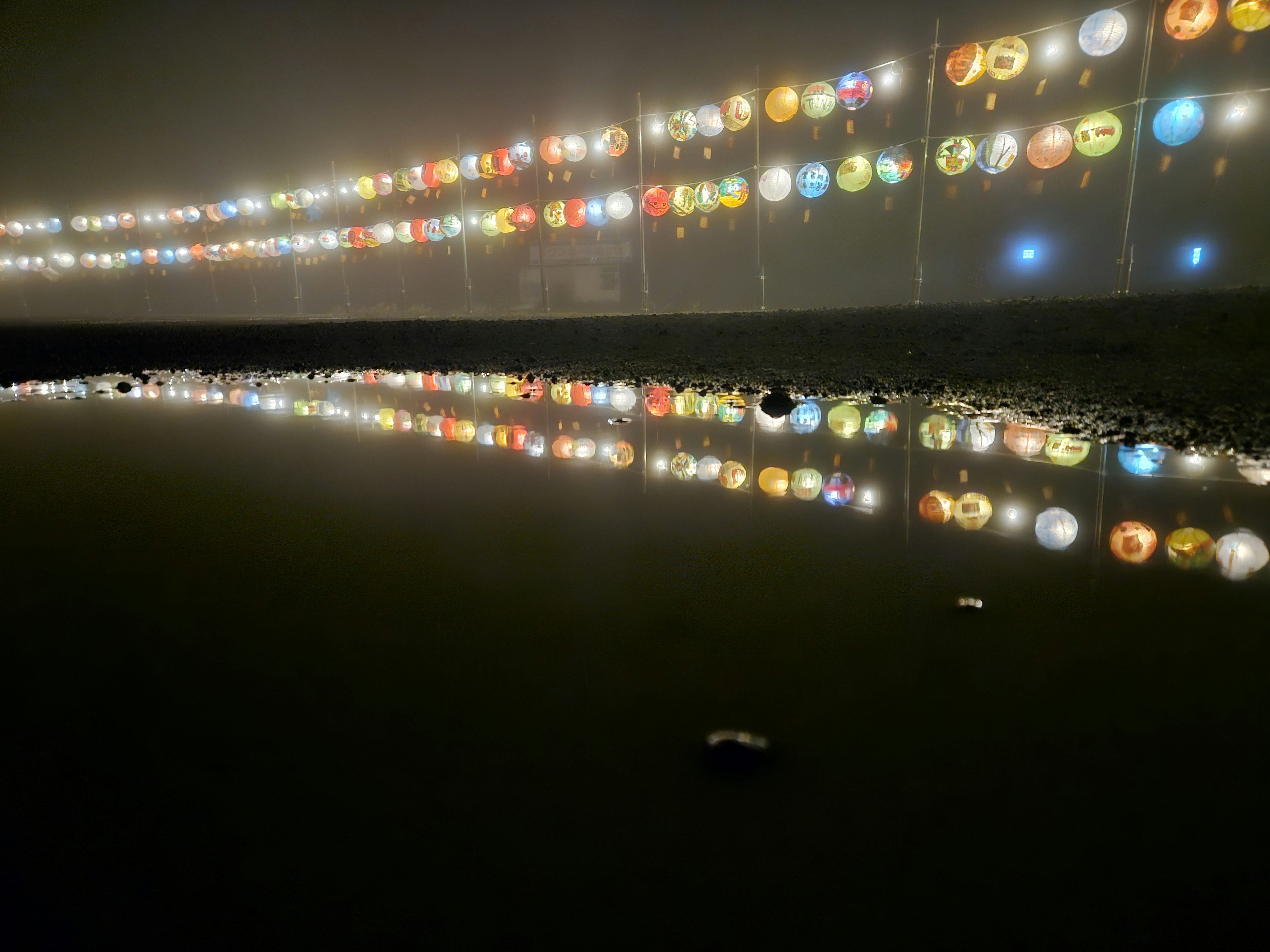 Faroles coloridos brillando en la niebla reflejados en un charco