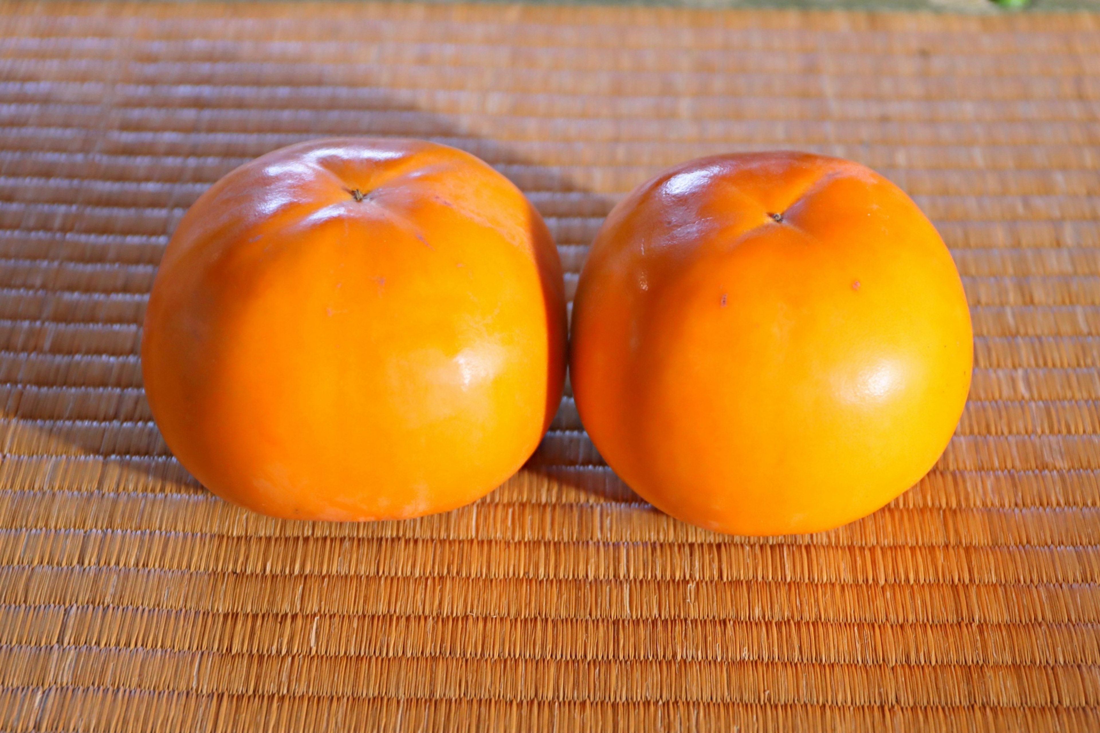 Dos caquis naranjas colocados sobre una estera de bambú