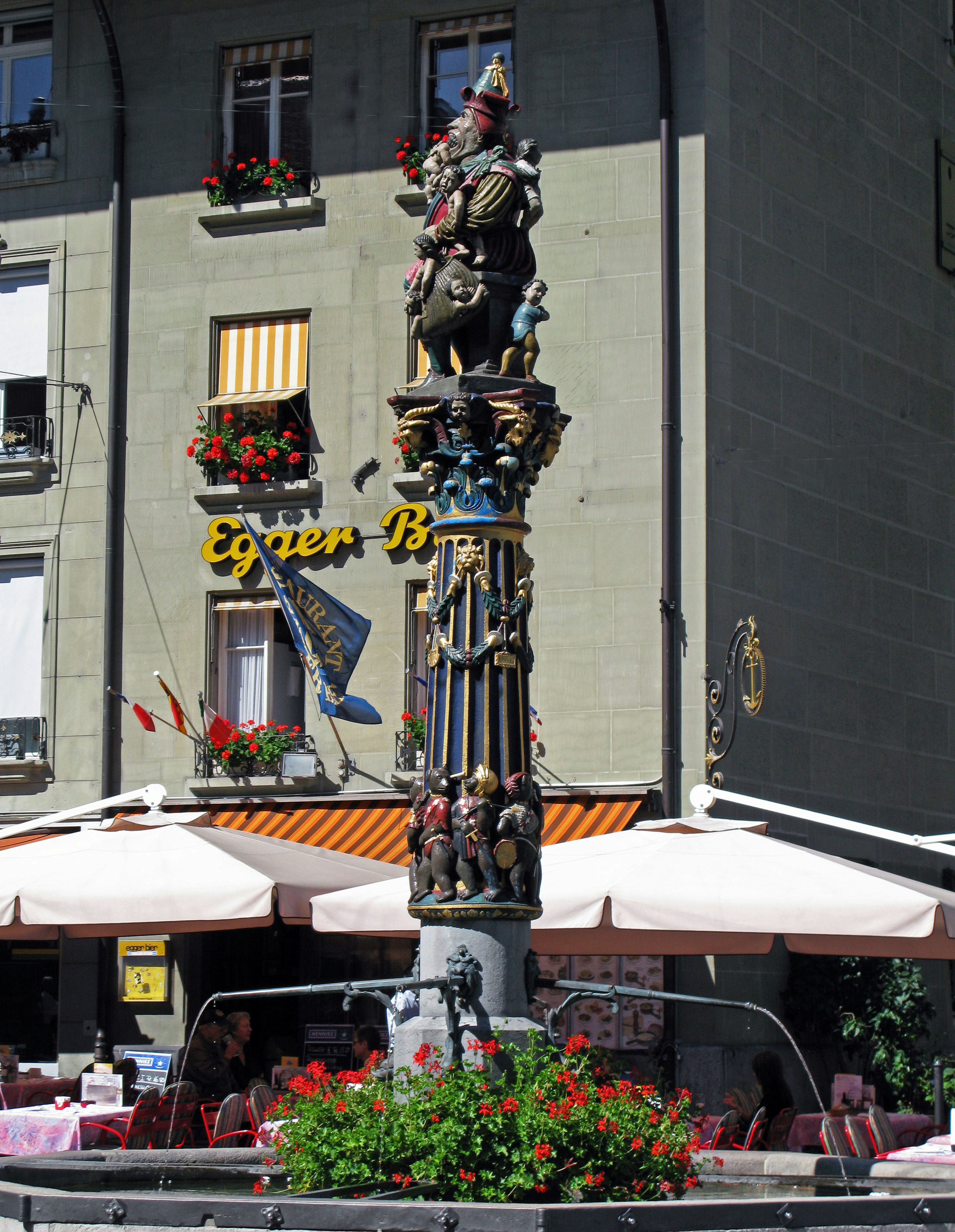 A beautifully carved fountain column with colorful flowers adorning a cafe terrace