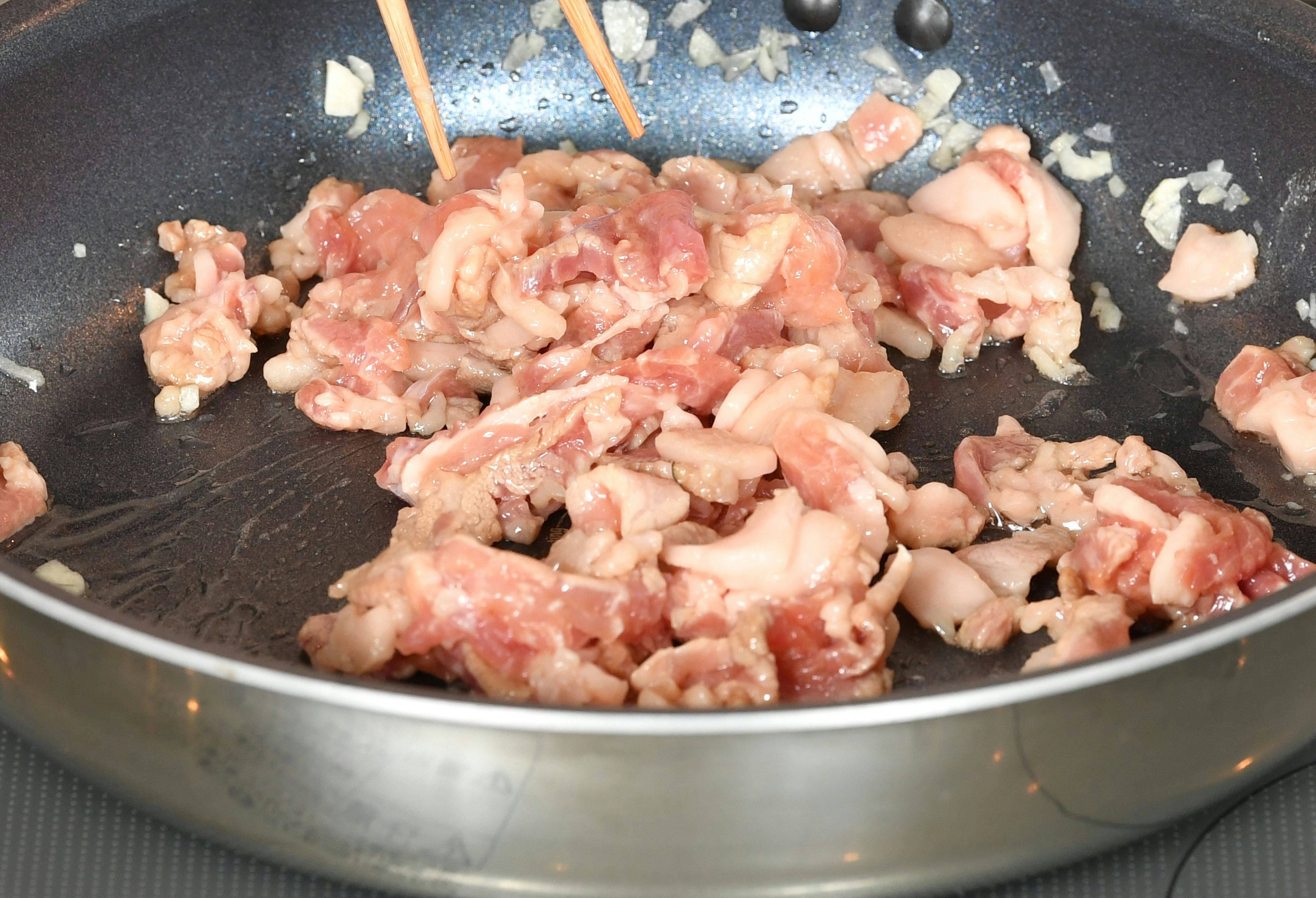 Porc tranché en train de cuire dans une poêle avec des baguettes