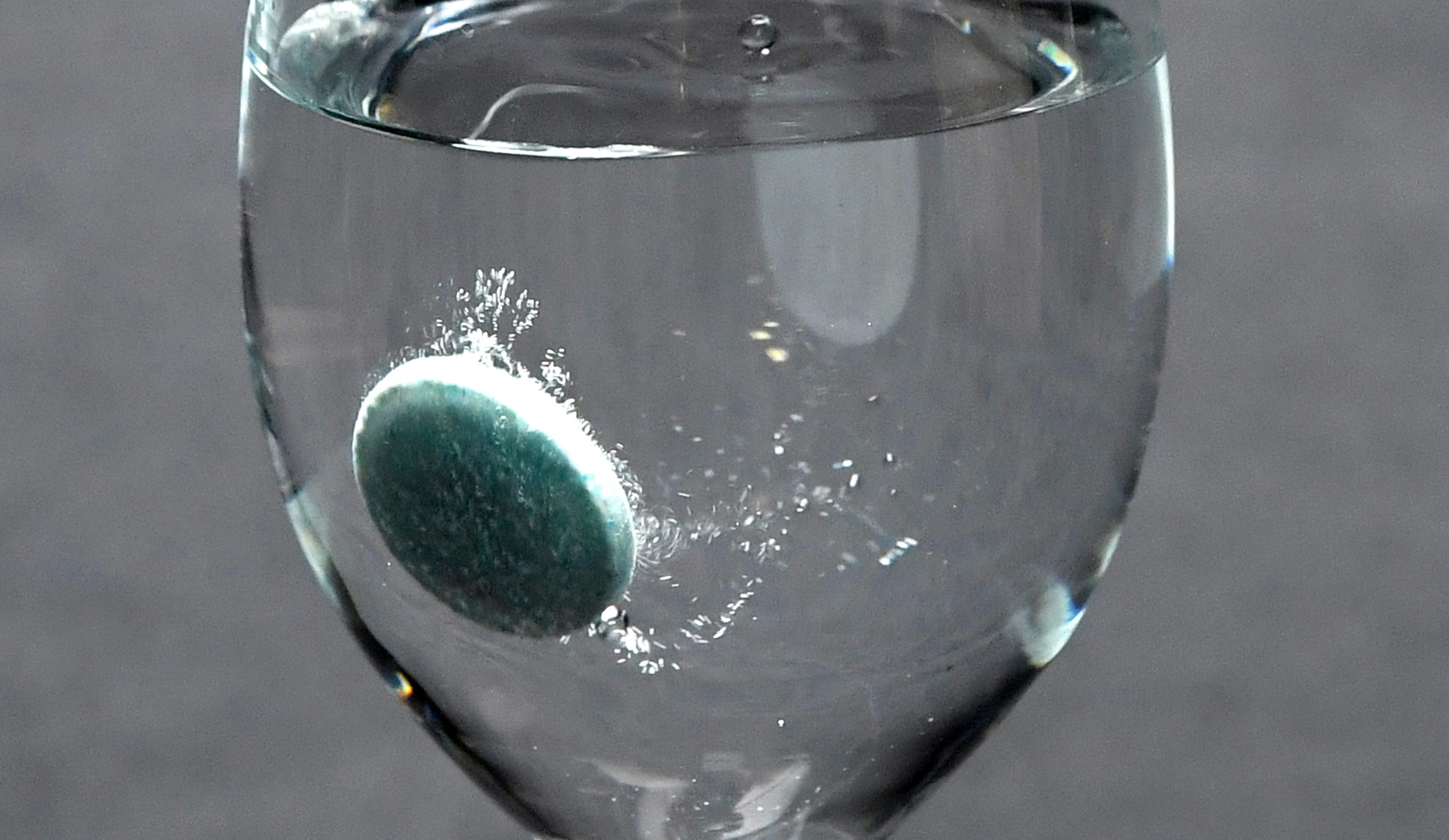 Blue-green tablet sinking in a glass of water